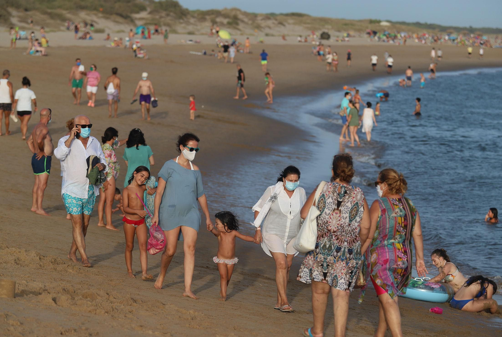 Varios grupos de personas pasean por una playa de la costa onubense al atardecer.