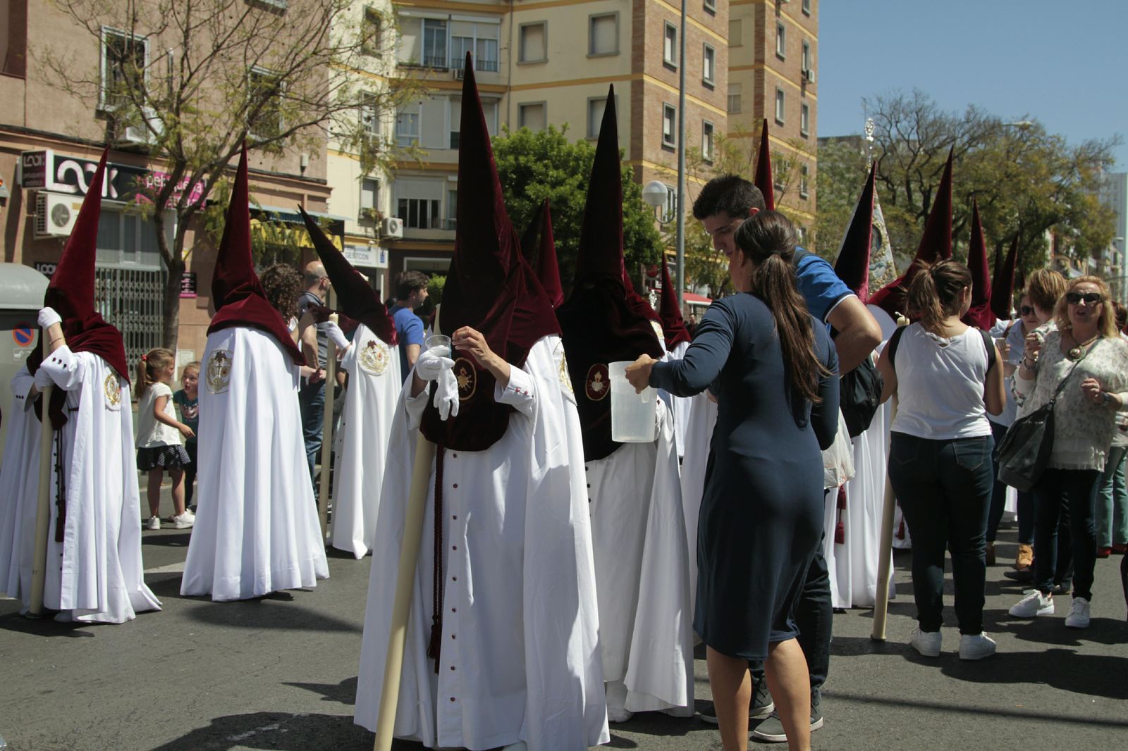 Una azafata de Emasesa lleva agua en una jarra a los nazarenos del Cerro.