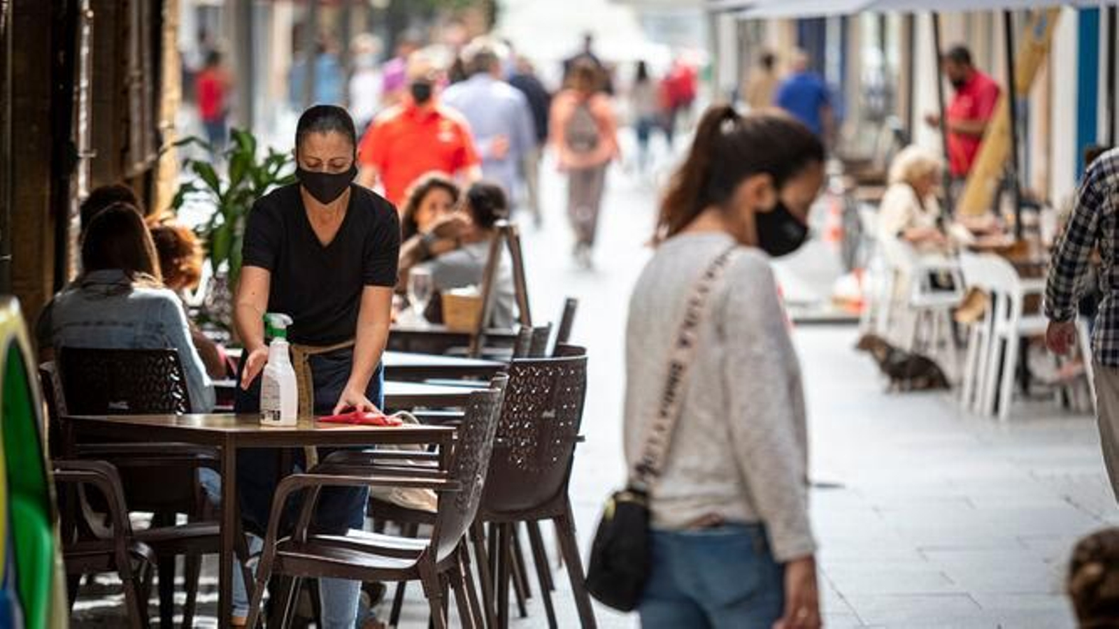 Una camarera limpia una mesa en una terraza de Cádiz.