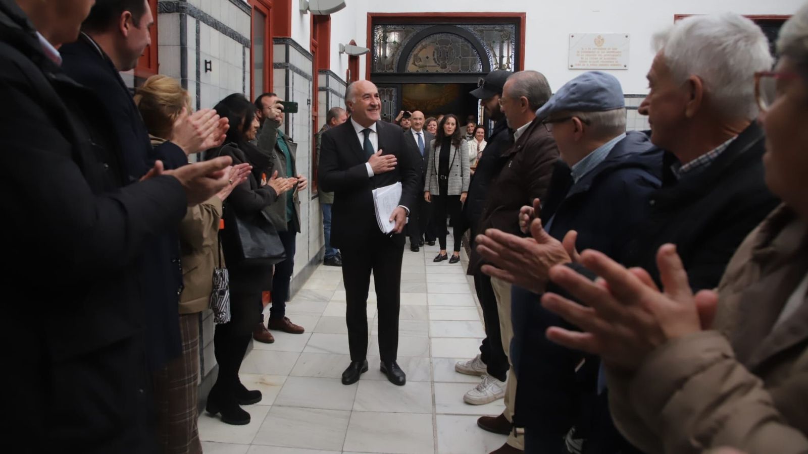 Landaluce accede al salón de Plenos con gesto sereno y la mano derecha sobre el pecho, seguido de sus concejales y acompañado por el aplauso de los asistentes.