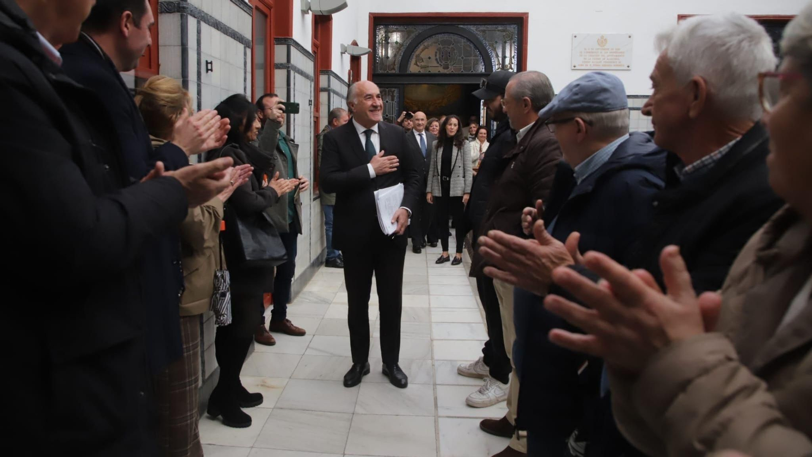 Landaluce accede al salón de Plenos con gesto sereno y la mano derecha sobre el pecho, seguido de sus concejales y acompañado por el aplauso de los asistentes.