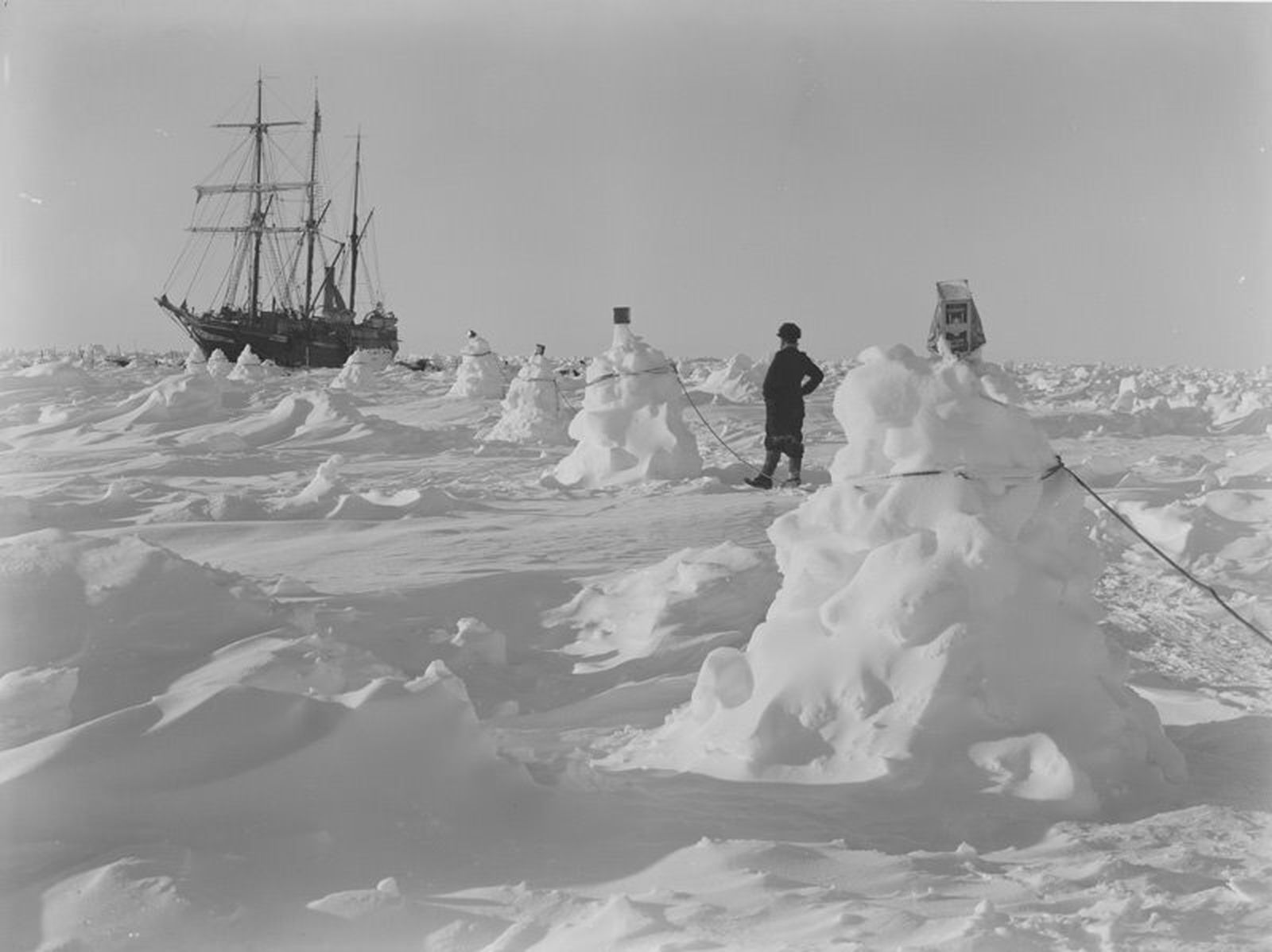Montones de nieve unidos con cuerdas para servir de guía en las ventiscas, con el 'Endurance' al fondo'