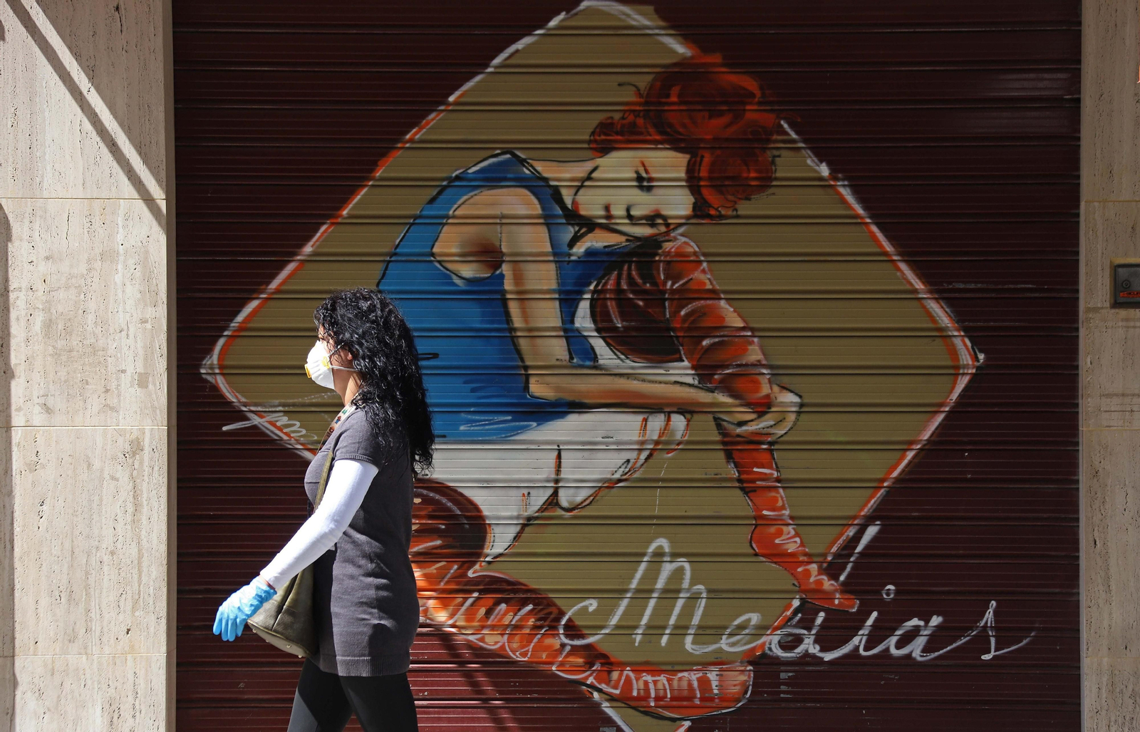 Una mujer con mascarilla pasa por un comercio cerrado en Algeciras.