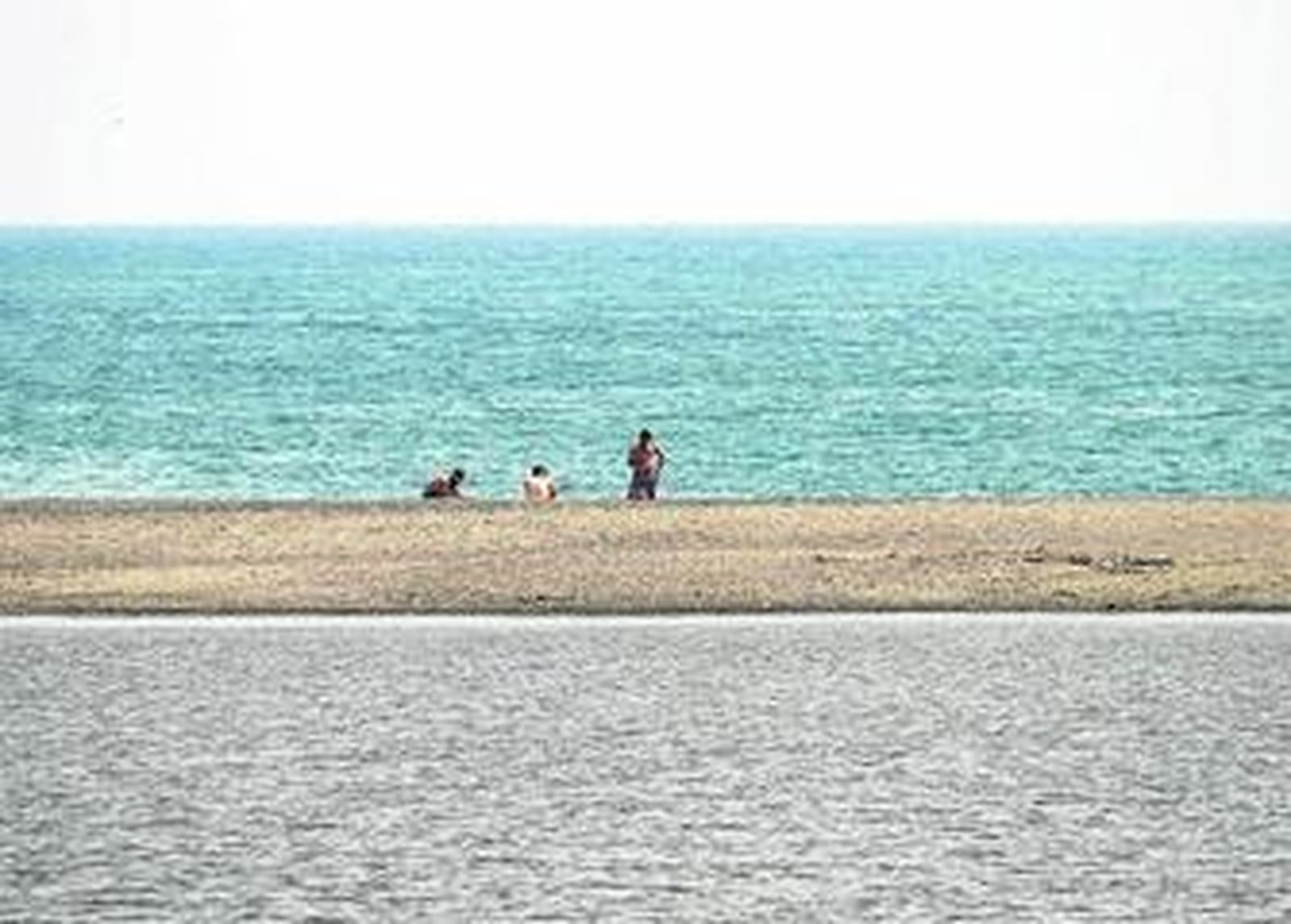 Tres bañistas entre la playa y la barrera de arena del Guadiaro, la pasada semana.