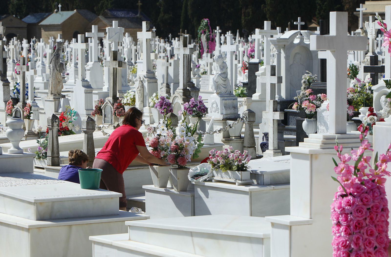 Dos mujeres colocan flores en la tumba de un fallecido.