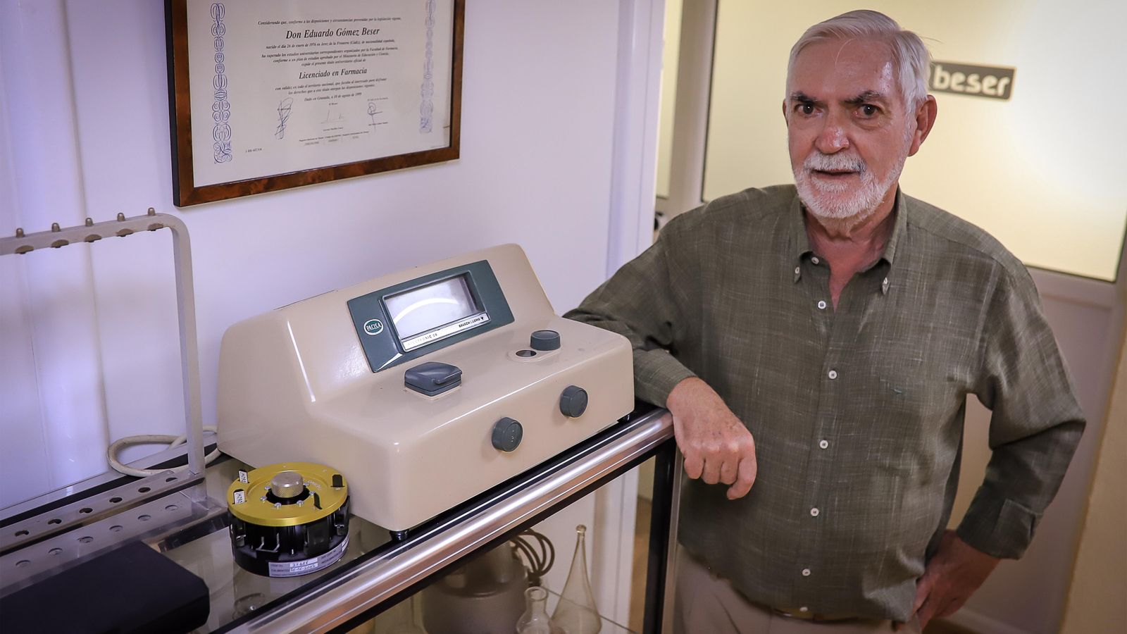 El farmacéutico, junto a una vitrina de objetos antiguos de la farmacia.