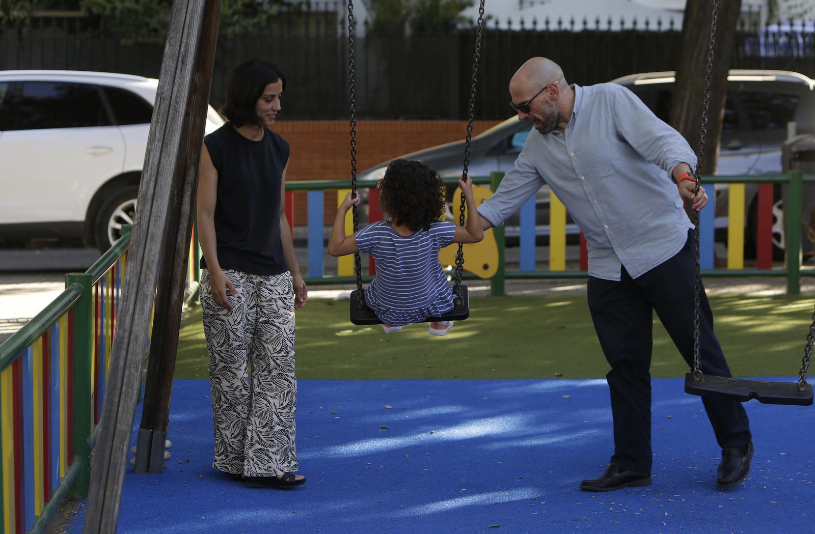 La pequeña Alba se pasea en el columpio de un parque infantil cerca de casa junto a sus padres.