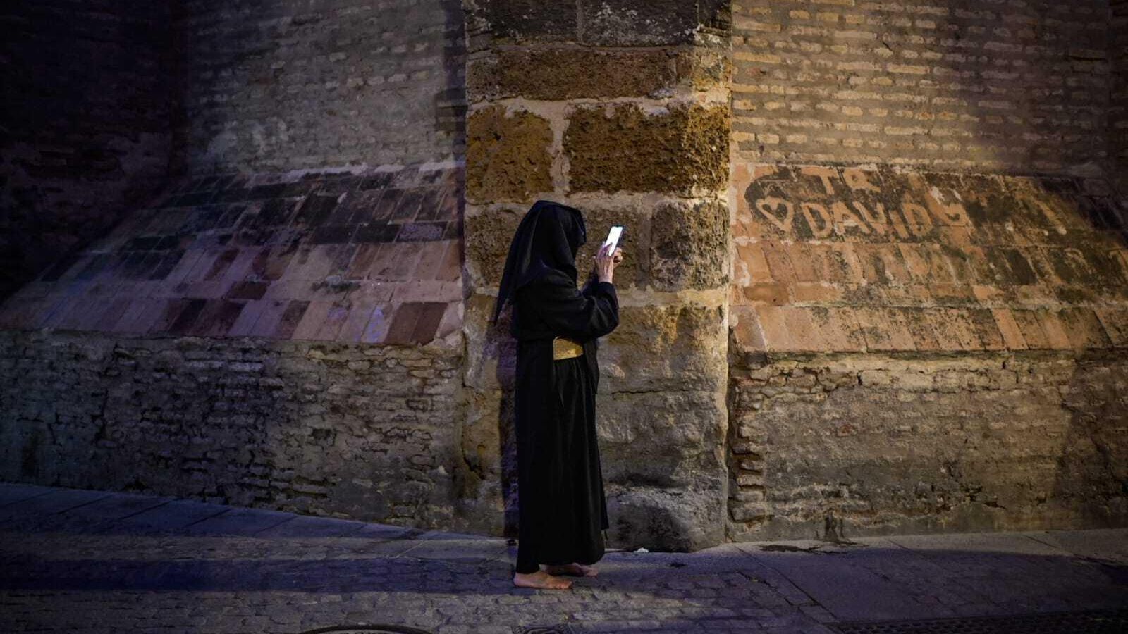 Un hermano de los Javieres mira el móvil tras suspenderse su estación de penitencia.
