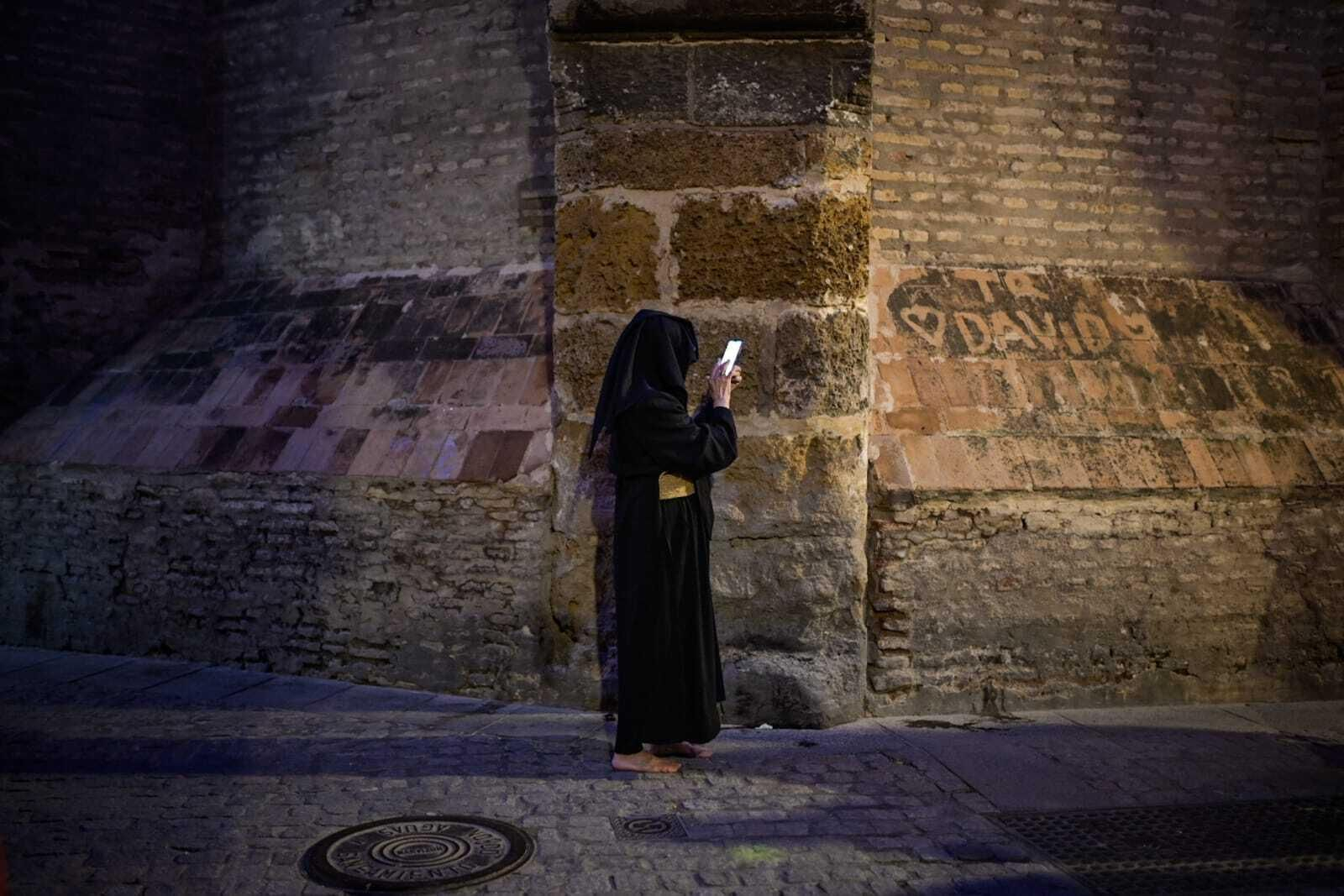 Un hermano de los Javieres mira el móvil tras suspenderse su estación de penitencia.