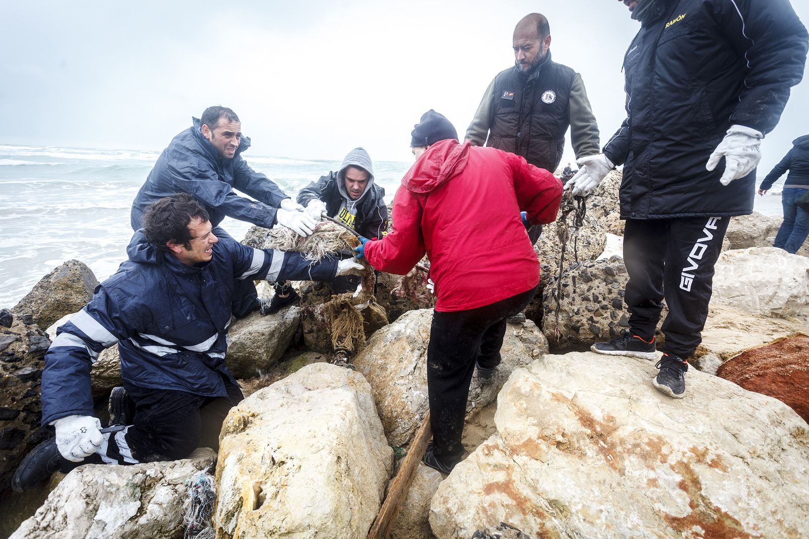 Rodeado de voluntarios, el alcalde ayuda a sacar unos restos de basura arrojada entre las piedras por el temporal.