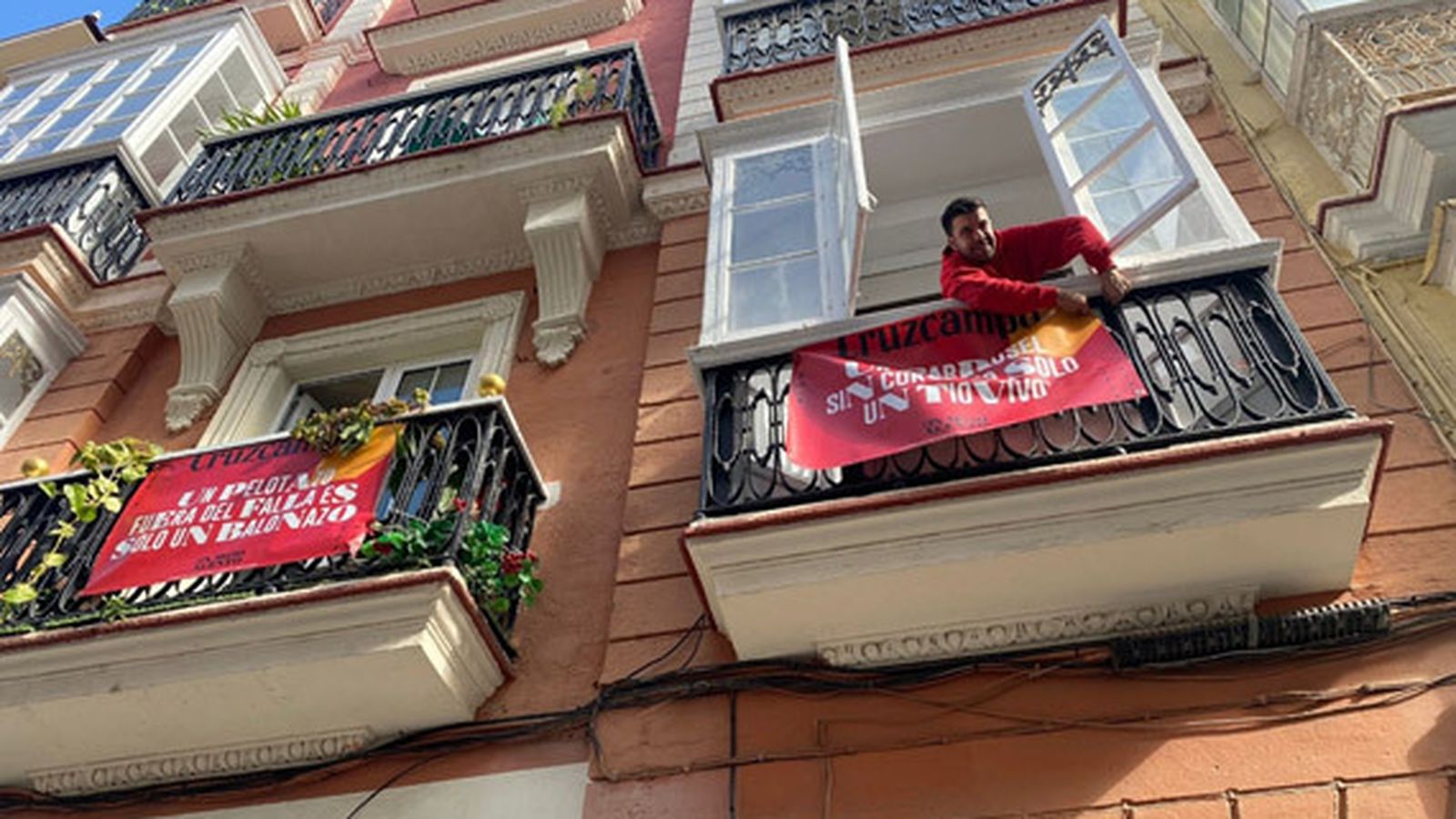 Un técnico de Cruzcampo coloca una bandelora con el mensaje 'Un carrusel sin coro es sólo un tiovivo' en un balcón del casco histórico de Cádiz.