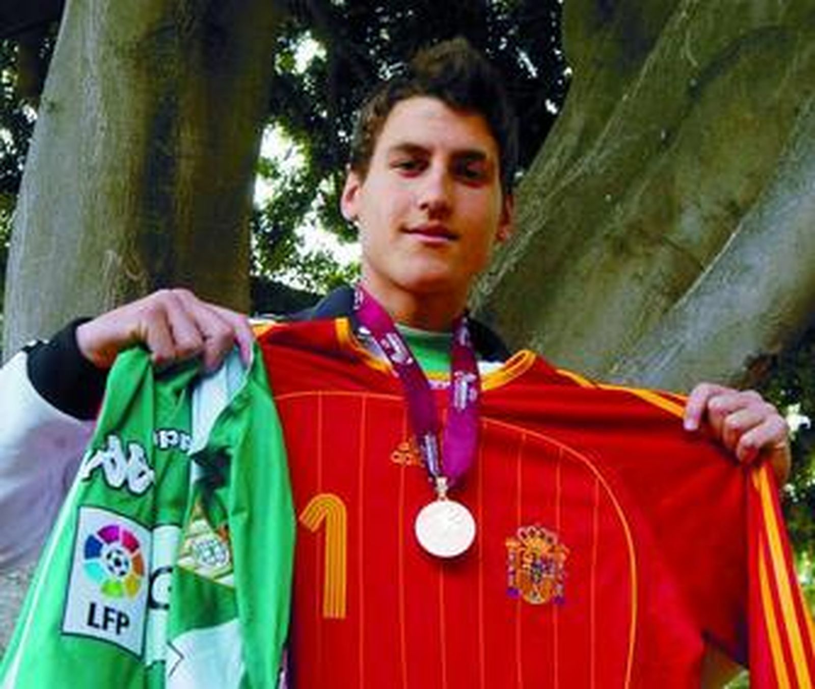 Manu posa con la medalla obtenida en el Europeo junto a las elásticas de la selección y el Betis.