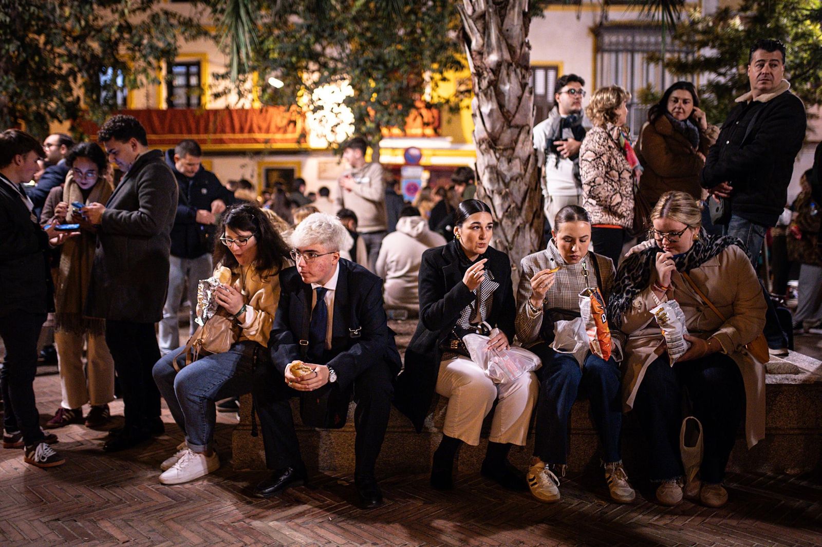 Jóvenes comiendo bocadillos y patatas a la espera de la llegada del Gran Poder a la Plaza de San Lorenzo.