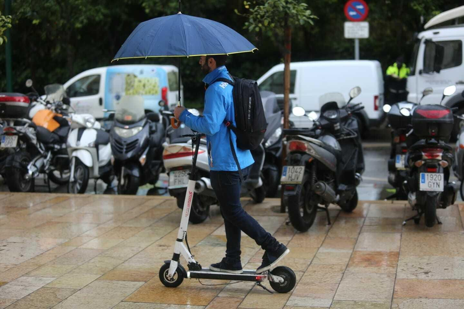 Un hombre se desplaza en patinete bajo la lluvia. Un hombre se desplaza en patinete bajo la lluvia.