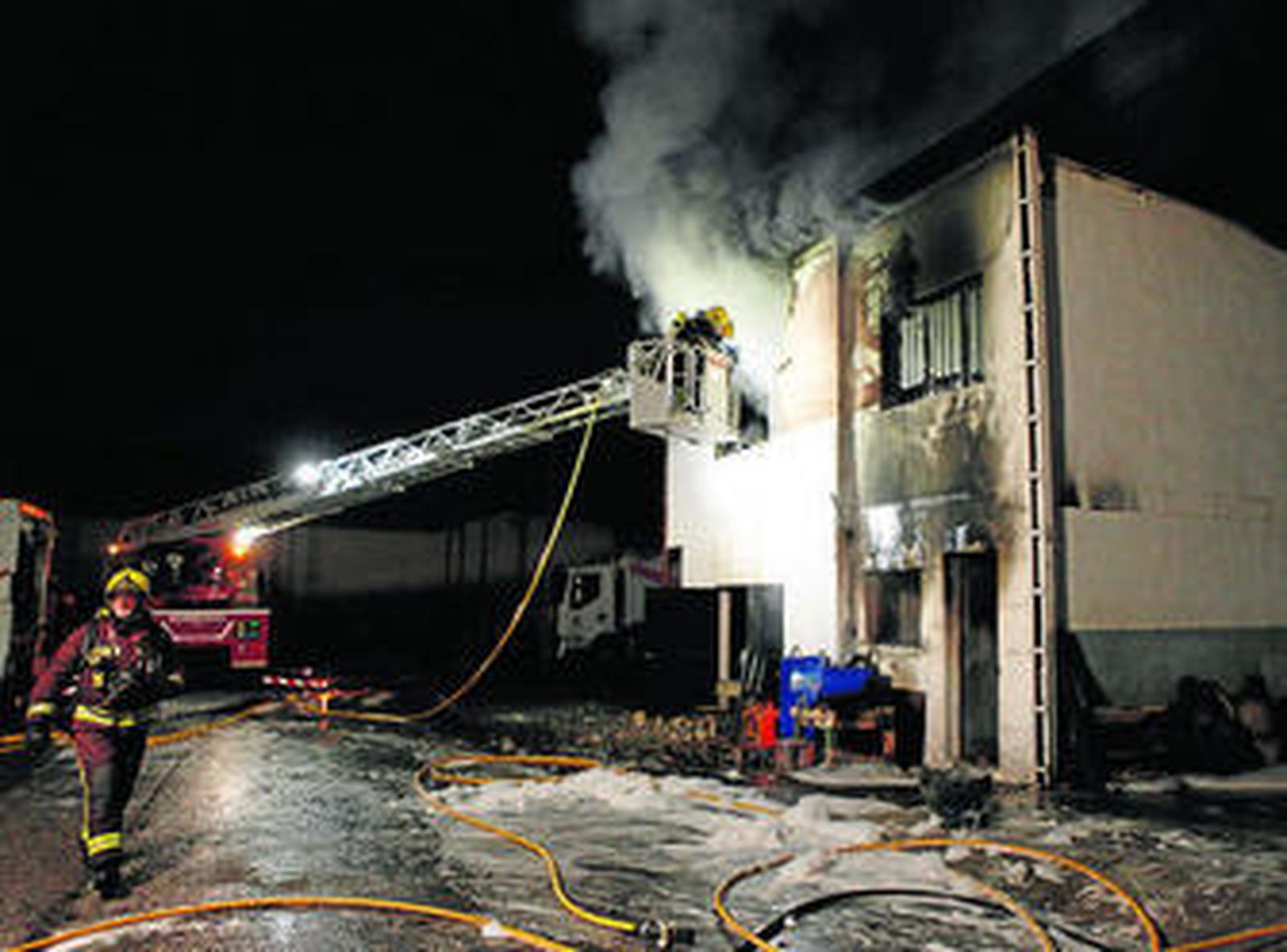 Los bomberos, desde una de las escaleras, tratan de apagar las llamas.