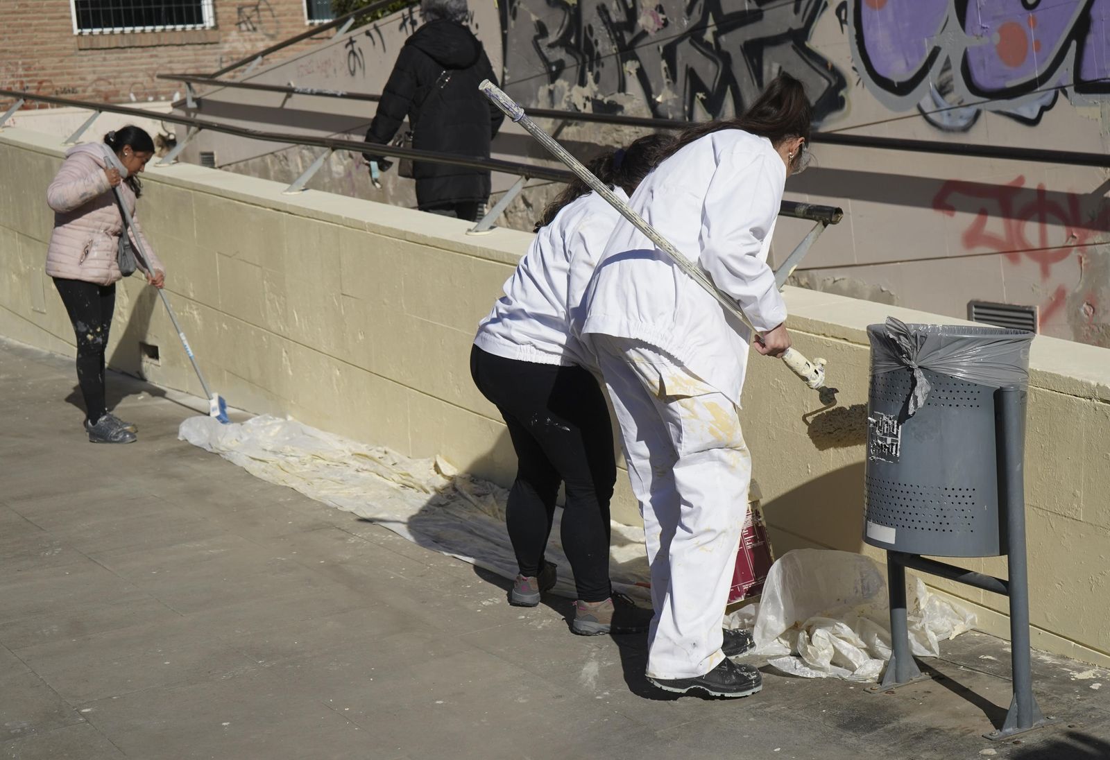 Tres personas limpian un muro para eliminar los grafitis existentes