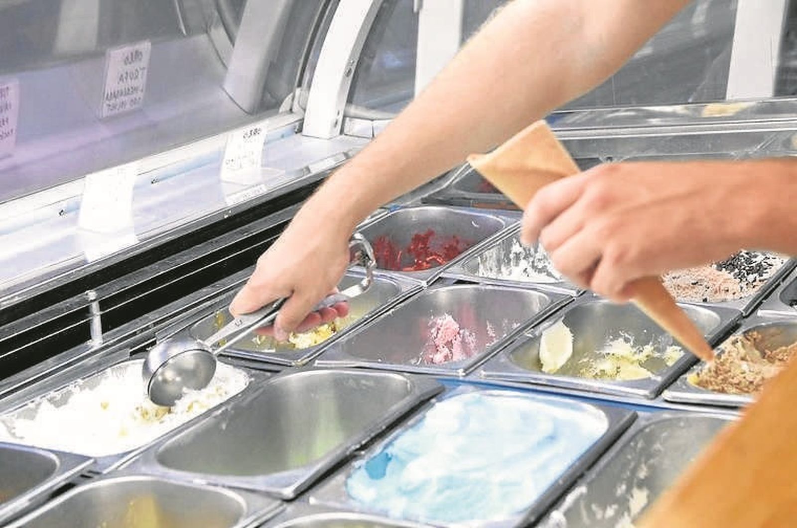 Un heladero sirve un cucurucho a un cliente.