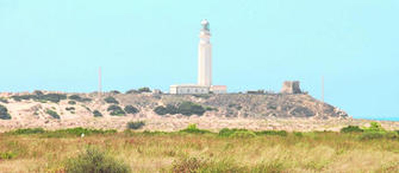 Vista de los terrenos que han sido objeto de una larga tramitación urbanística. Al lado, el faro visto desde la playa de Zahora, con numerosos bañistas.