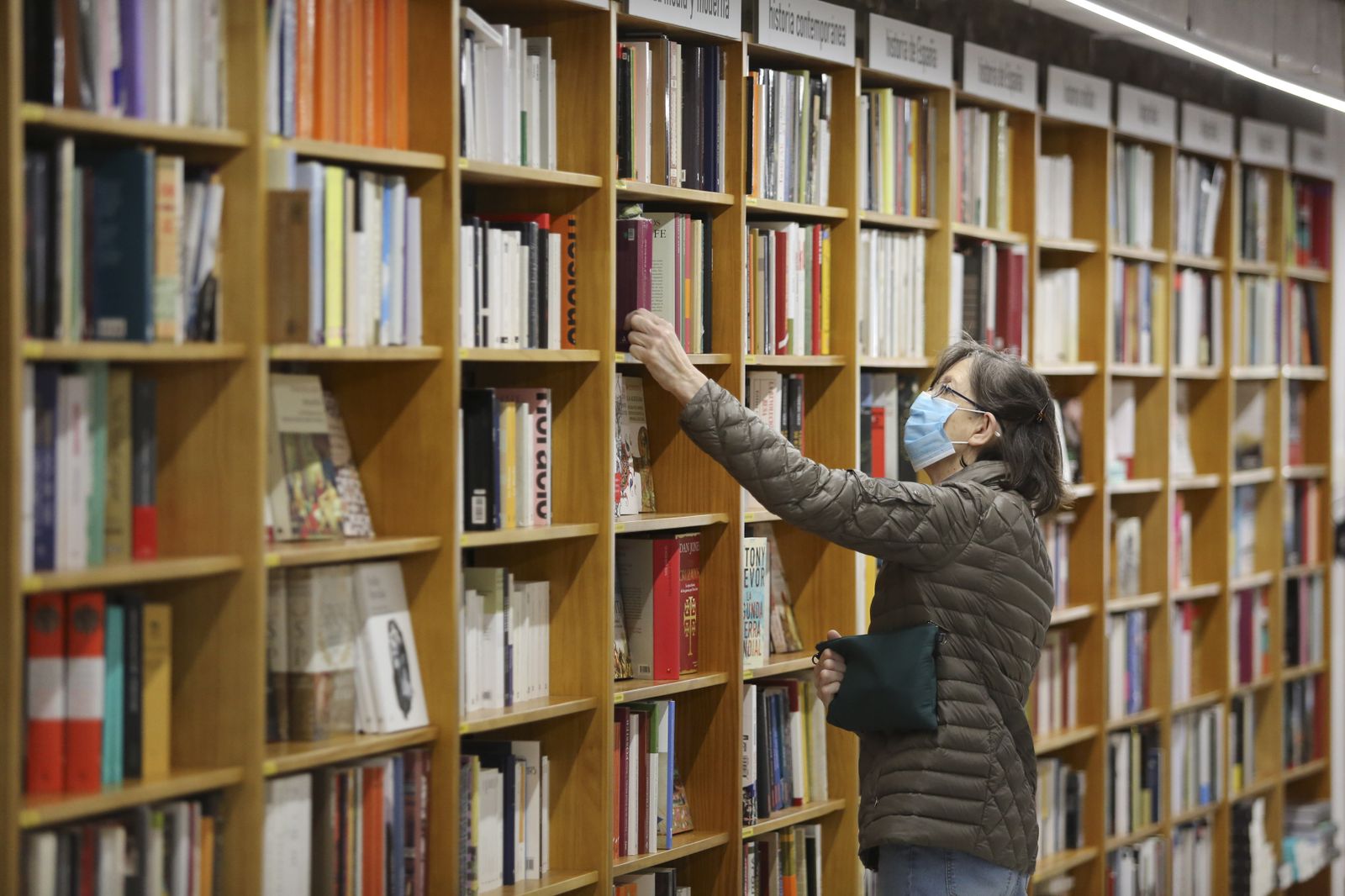 Una lectura consulta los volúmenes de una estantería en la Librería Luces.