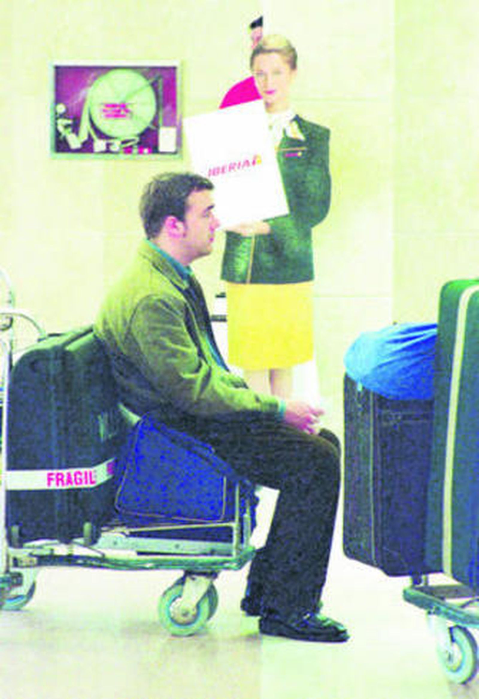 Un pasajero en cola sentado sobre su equipaje.