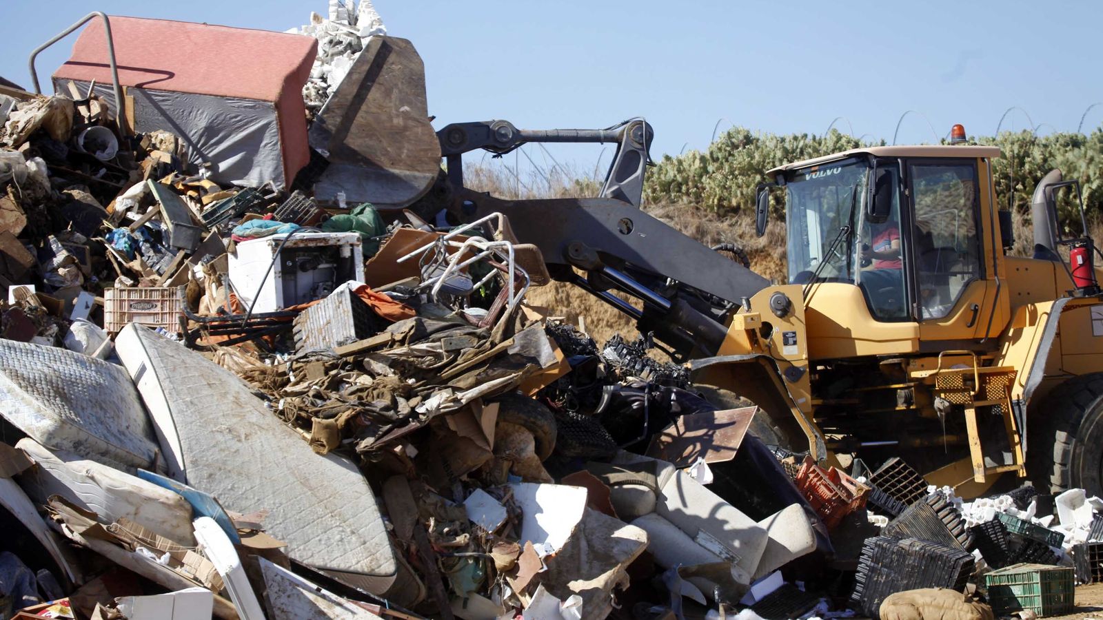 Una retroexcavadora amontona los enseres que han quedado inutilizados por el agua y el lodo