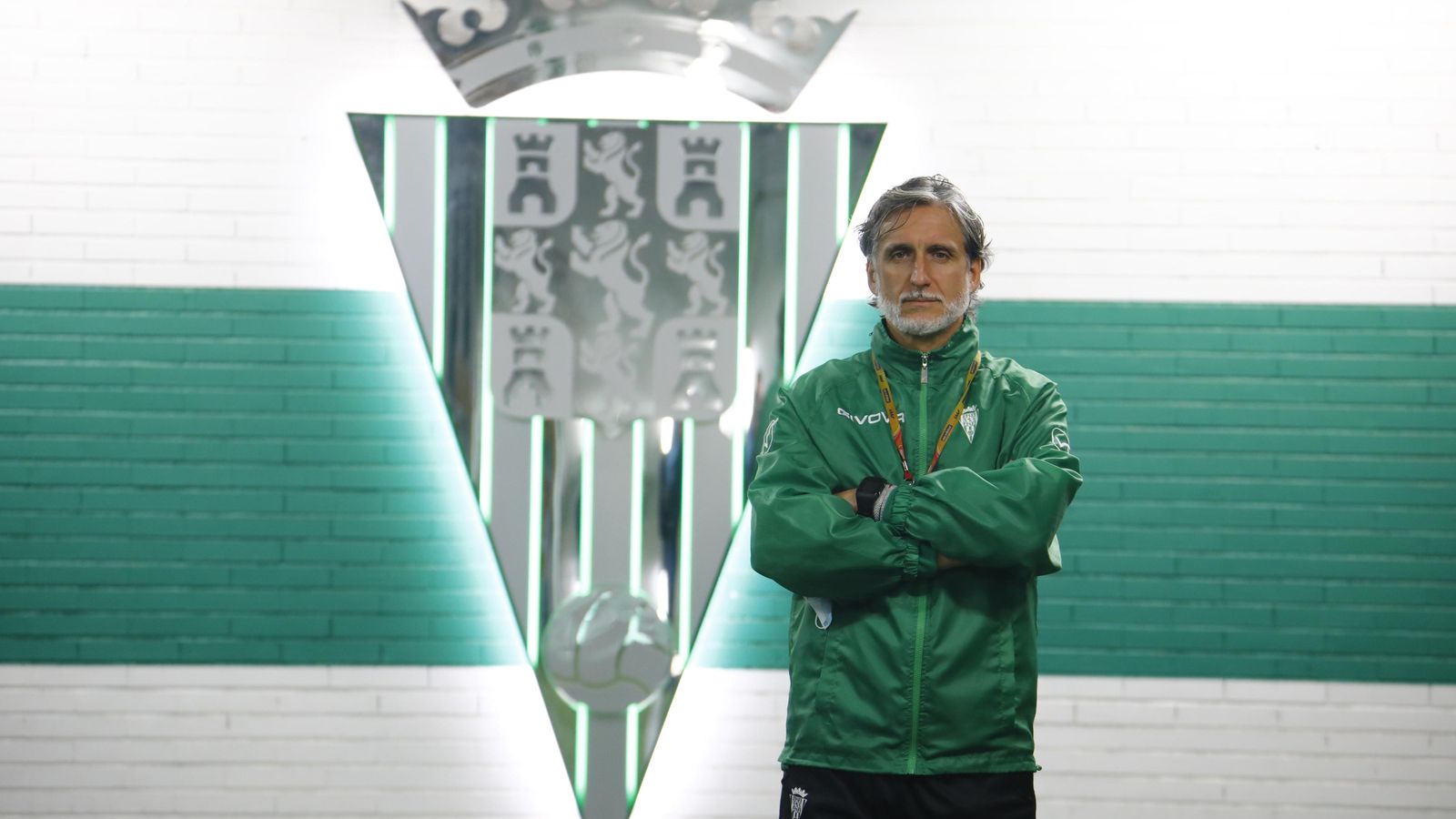 El técnico posa junto al escudo que preside el acceso al césped de El Arcángel.