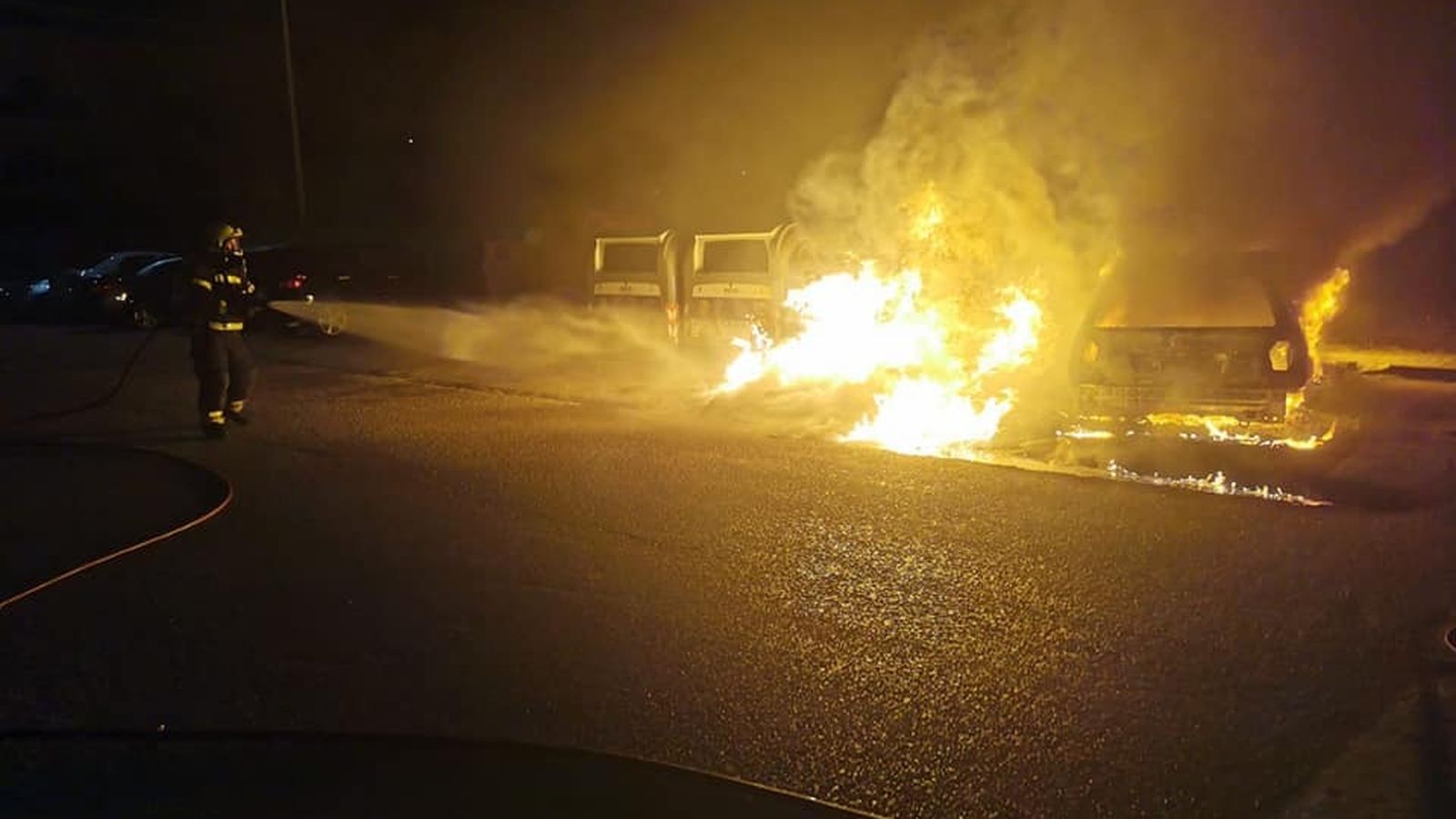Un bombero apaga un coche incendiado.