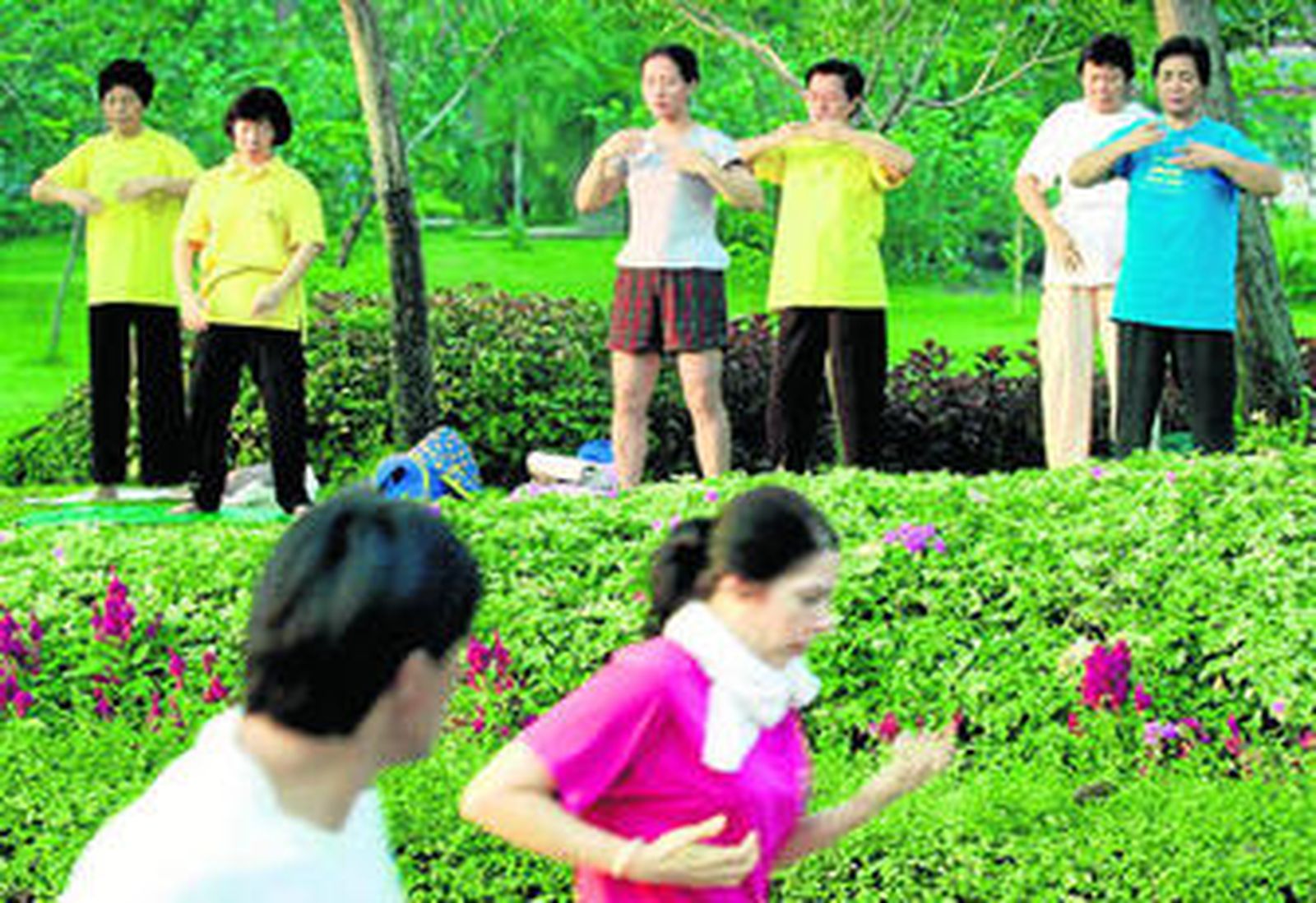 Dos personas realizan ejercicio físico frente a un grupo que medita en un parque de Bangkok.