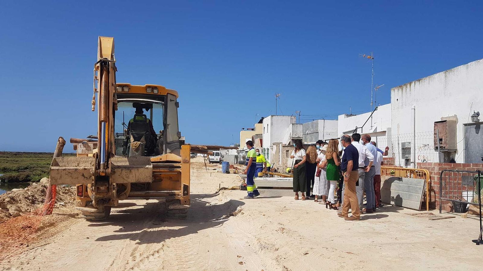 Una excavadora pasa junto al grupo del representantes municipales y vecinales en La Almadraba.