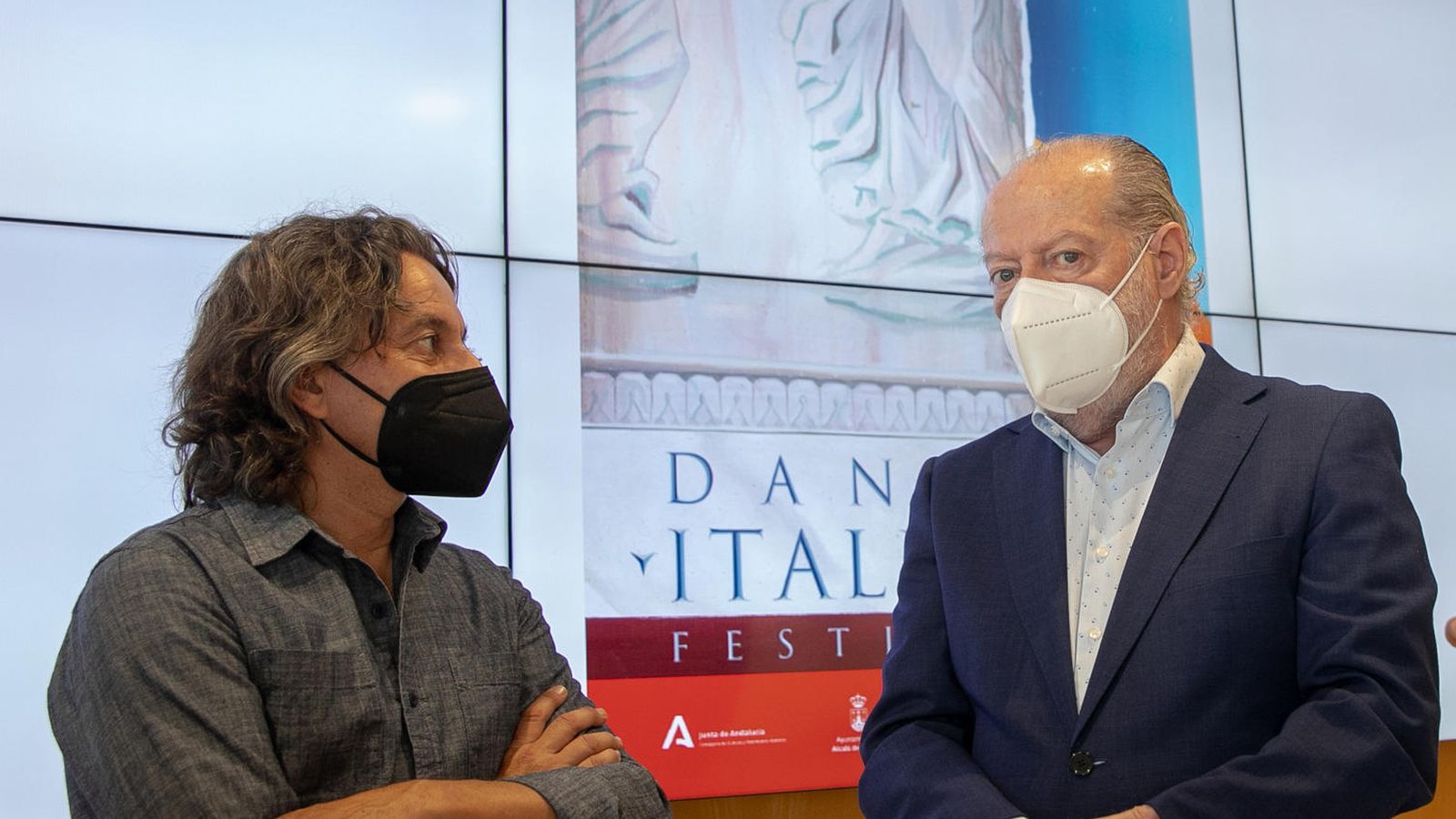 Javier Barón conversa con el presidente de la Diputación de Sevilla, Fernando Rodríguez Villalobos, ante el cartel de Itálica diseñado por Gloria Martín.