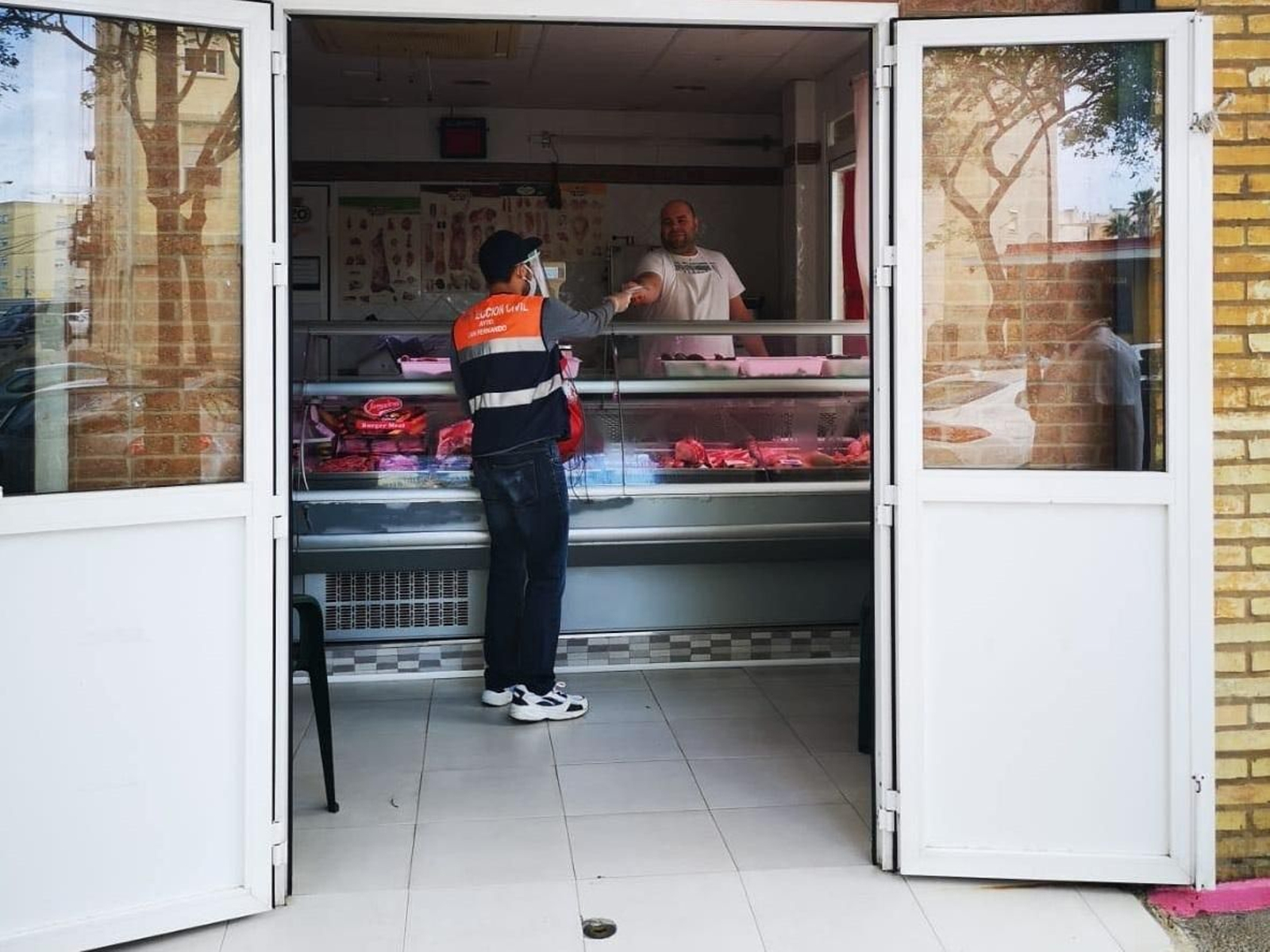 Voluntarios de Protección Civil entregan mascarillas en una carnicería.