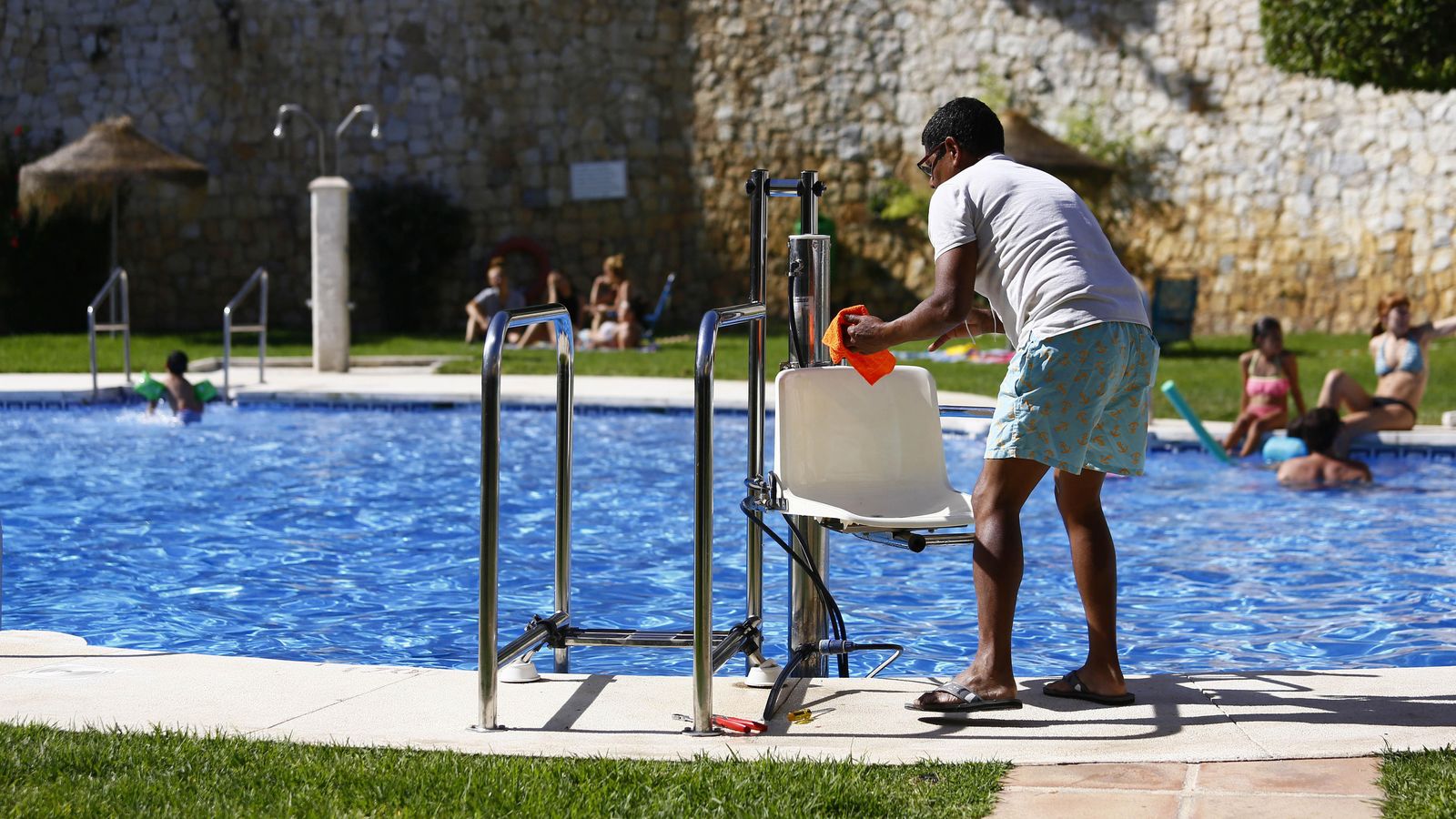 Un profesional de mantenimiento limpia la silla de discapacitados en una piscina de El Cantal.