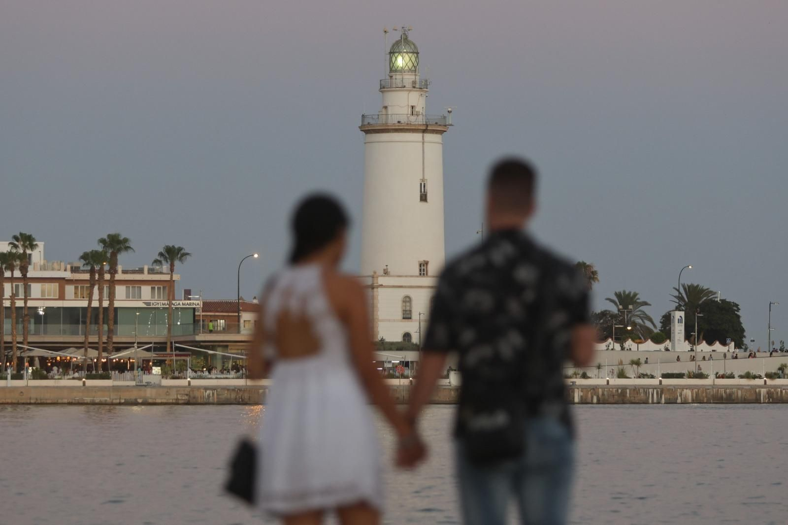 Una pareja pasea por el Puerto de Málaga, con la Farola de fondo.
