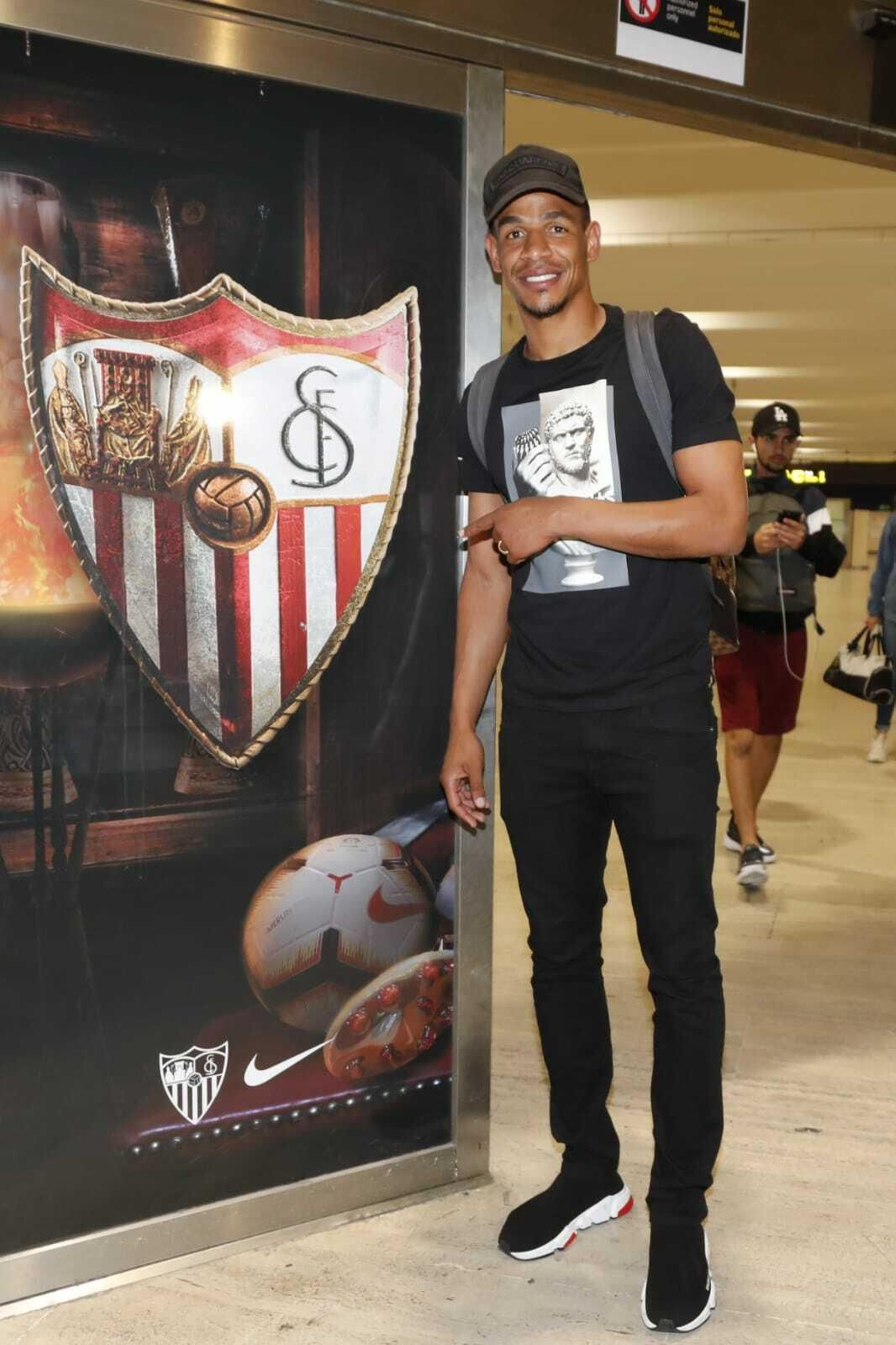 Fernando señala sonriente el escudo del Sevilla en la  puerta del aeropuerto.