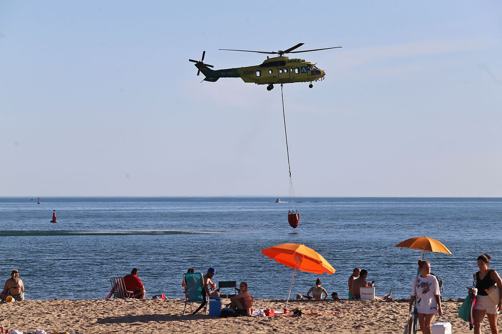 Un helicóptero del Infoca recoge agua en la playa de El Portil en presencia de bañistas este miércoles pasado.