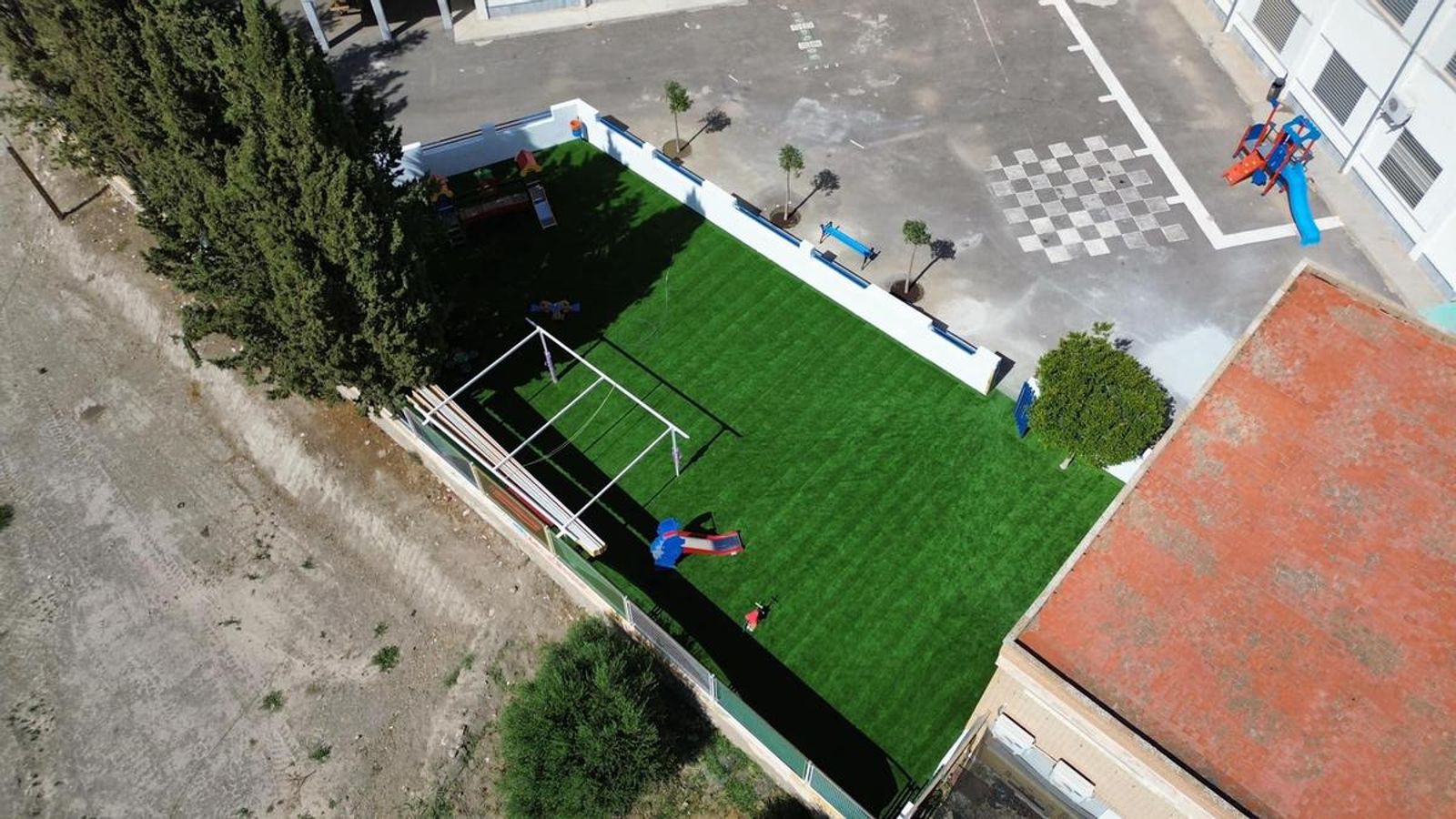 Vista aérea del parque infantil con el nuevo suelo de césped artificial, zona de juegos y árboles recién plantados
