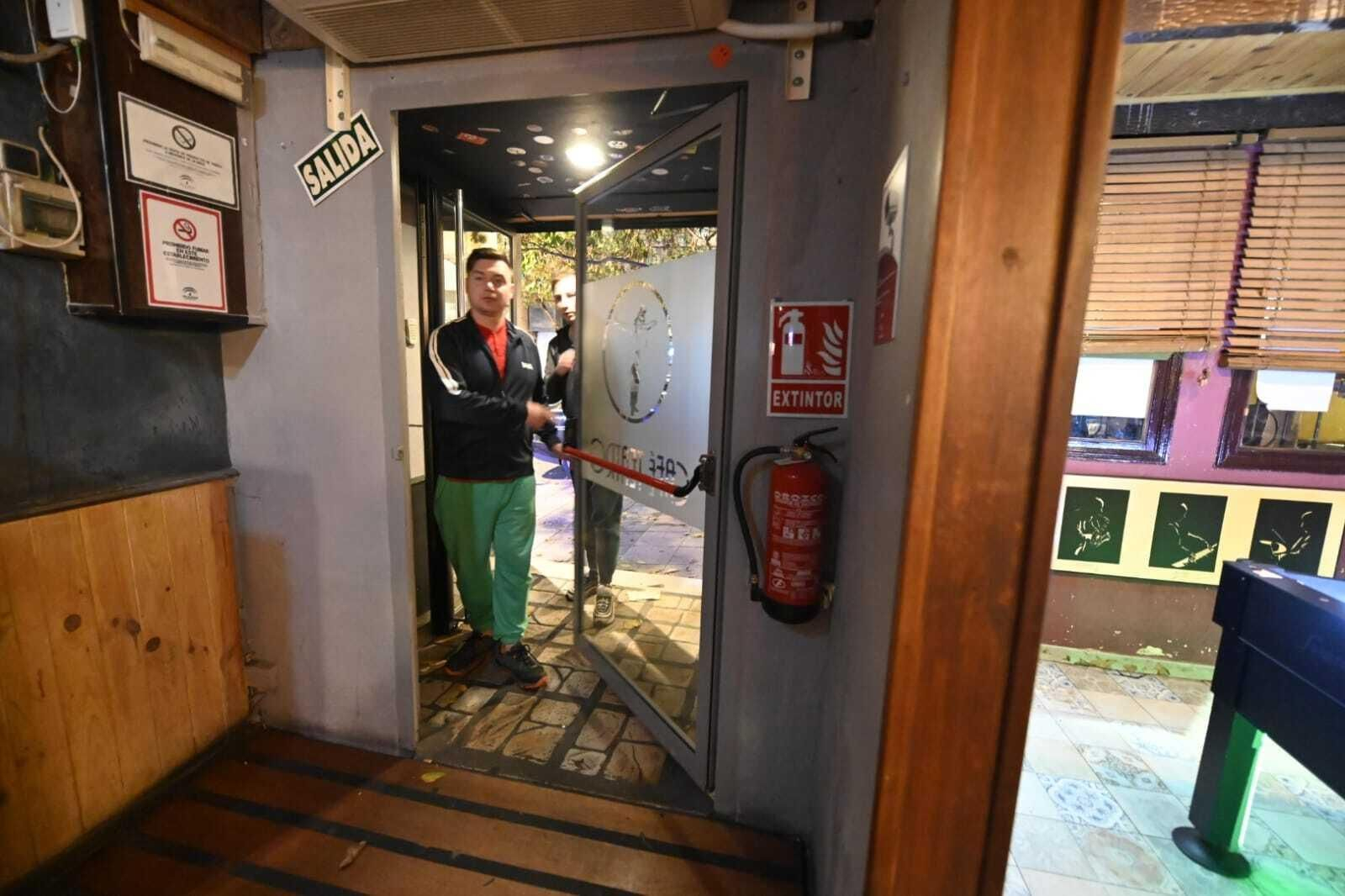 Una persona accede a un pub en el que se observan cartelería, extintores y una puerta antipánico.