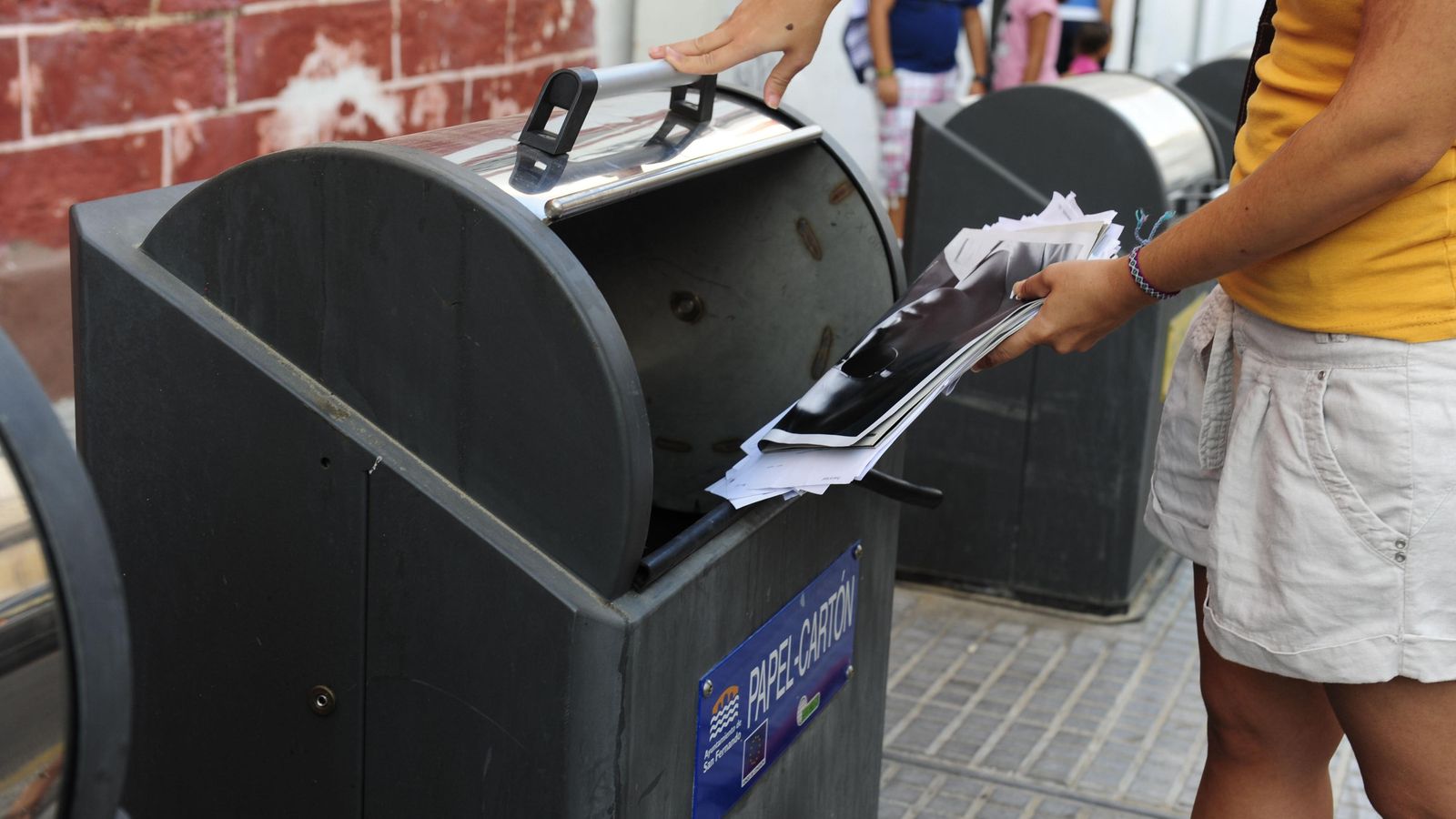 Una ciudadana recicla  papel en un contenedor específico.