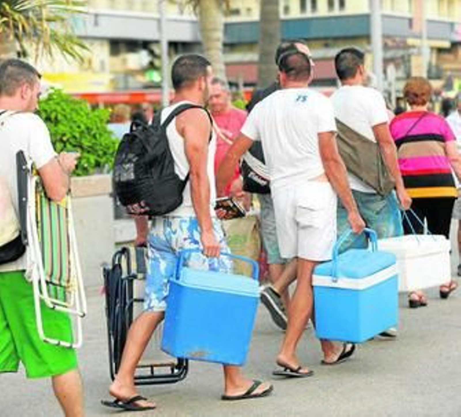Varios jóvenes se dirigen hacia la playa con neveras, sillas y mochilas.
