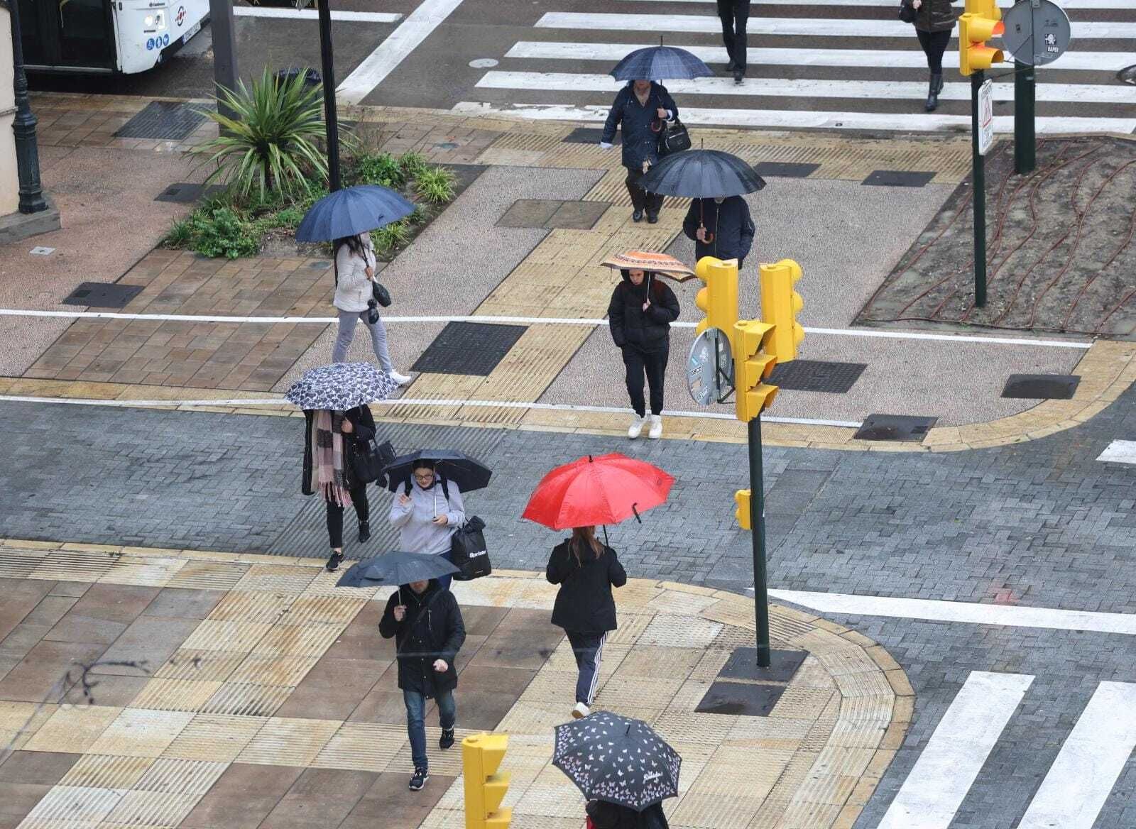 Peatones cruzan la Alameda Principal de Málaga protegidos por paraguas este miércoles.