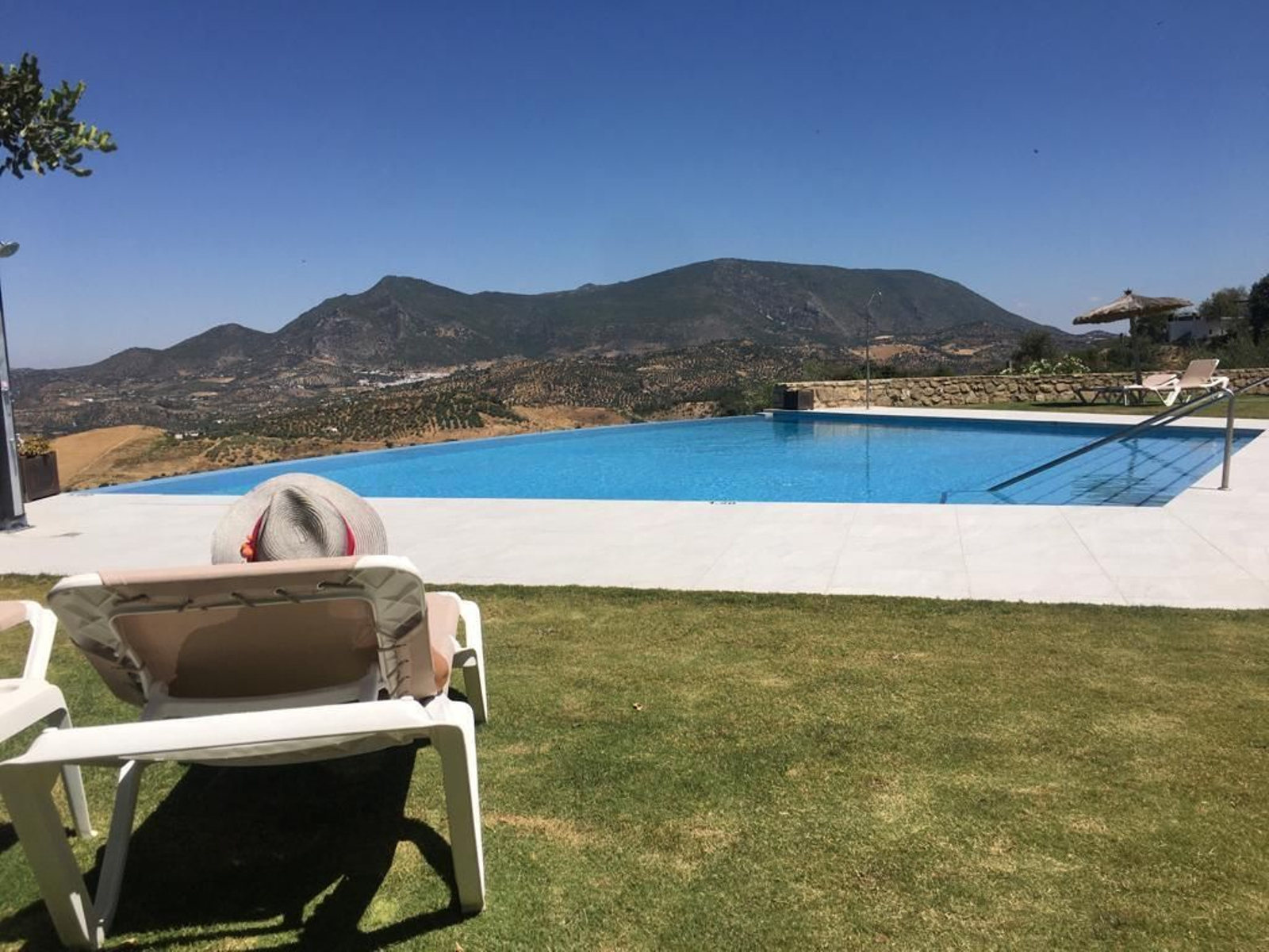 Una persona disfruta de las flamantes instalaciones de la piscina del Hotel Los Tadeos, en Zahara de la Sierra, con un paisaje de suaves montañas al fondo.