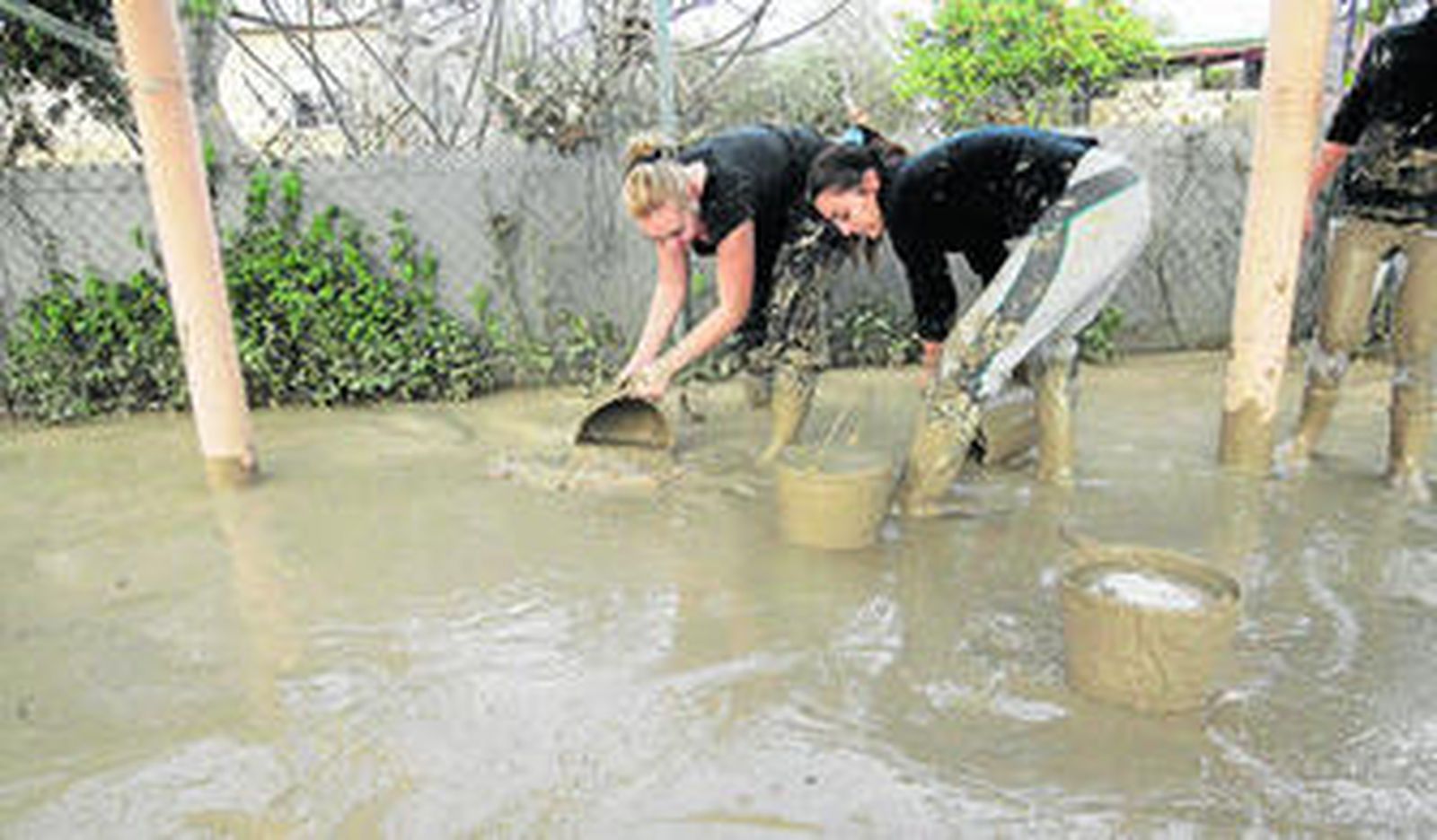 Dos mujeres se afanan a la retirada del lodo del jardín de su vivienda ayer domingo.