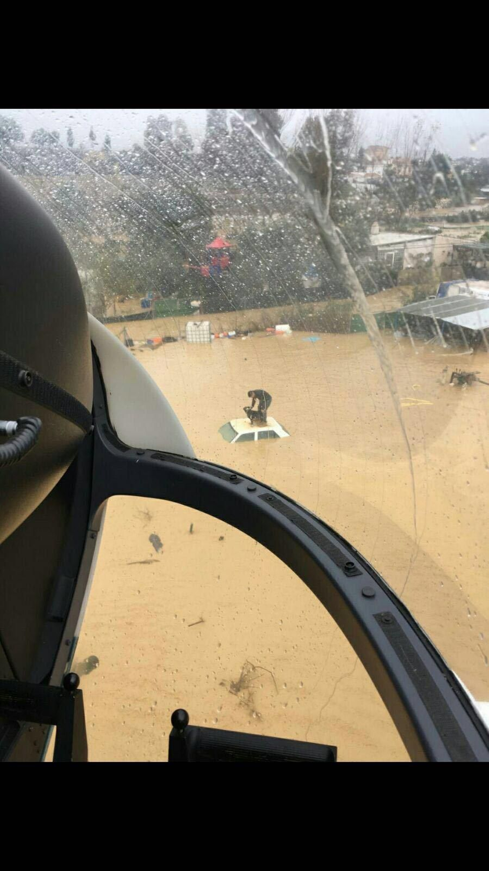 Un hombre subido con su perro al techo de su coche espera a ser rescatado.