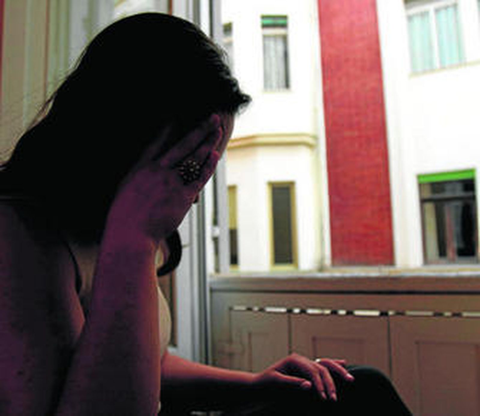 Una mujer con síntoma de depresión, asomada a la ventana de su casa.