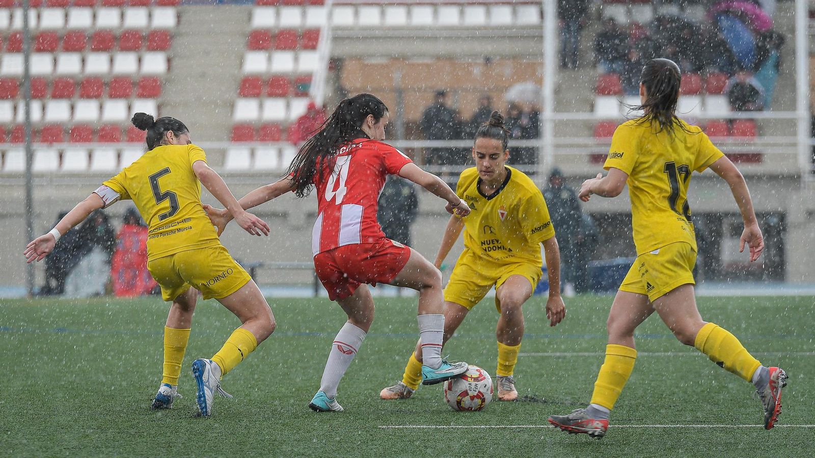 La rojiblanca Lucía presionada por hasta tres rivales durante una acción del encuentro mientras caía una importante lluvia.