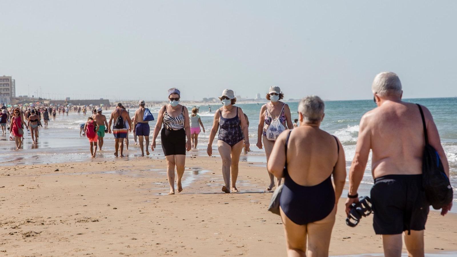 Personas pasean por la playa Victoria de Cádiz usando mascarillas.