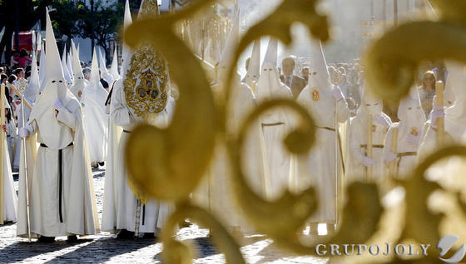 Las numerosas filas de nazarenos blancos de la hermandad del Transporte se adivinan entre las filigranas de sus insignias.

Foto: Miguel Angel Gonzalez