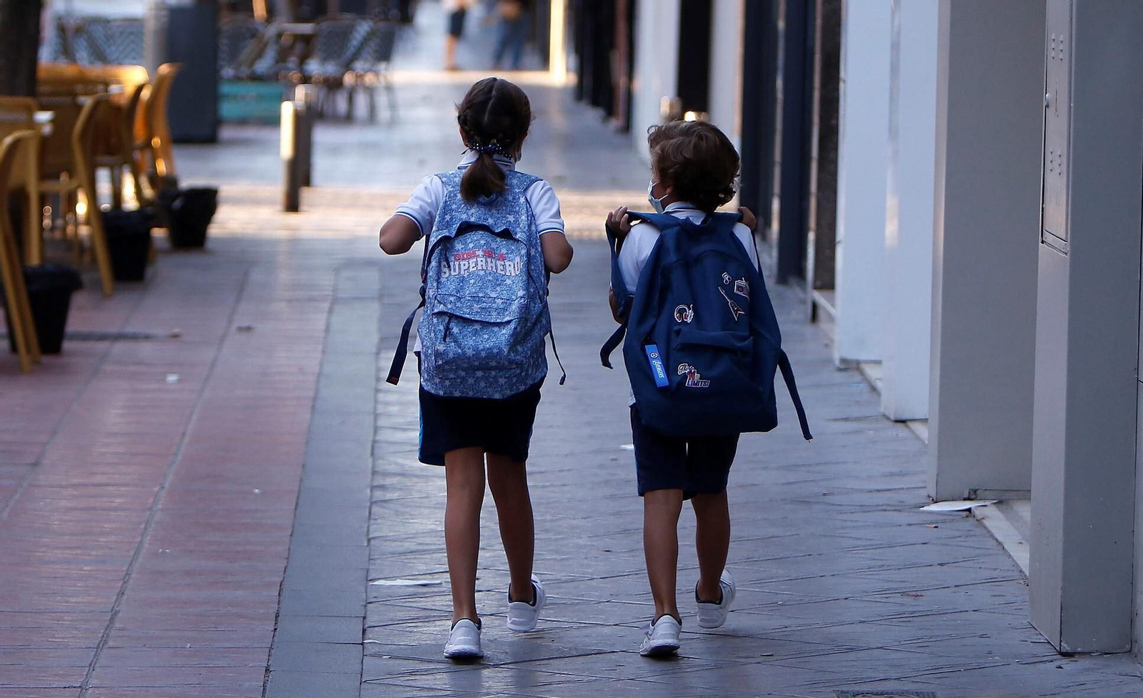 Dos niños caminan por una calle con sus mochilas.