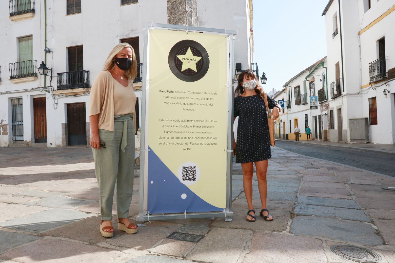 Isabel Albás y Lucía del Pino, junto al cartel situado en la plaza del Potro.