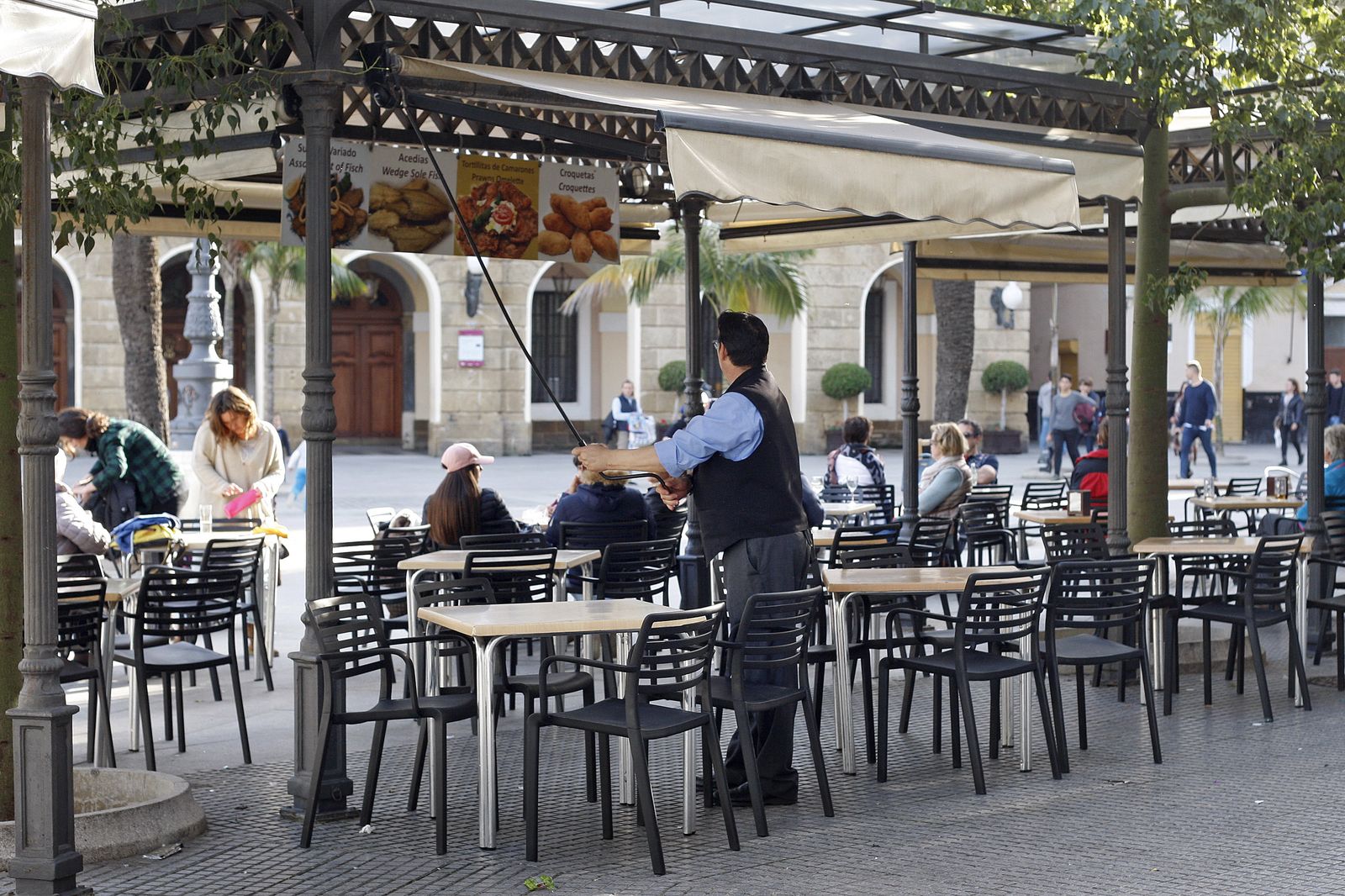 Un camarero recoge un toldo en un bar de la plaza de San Juan de Dios.